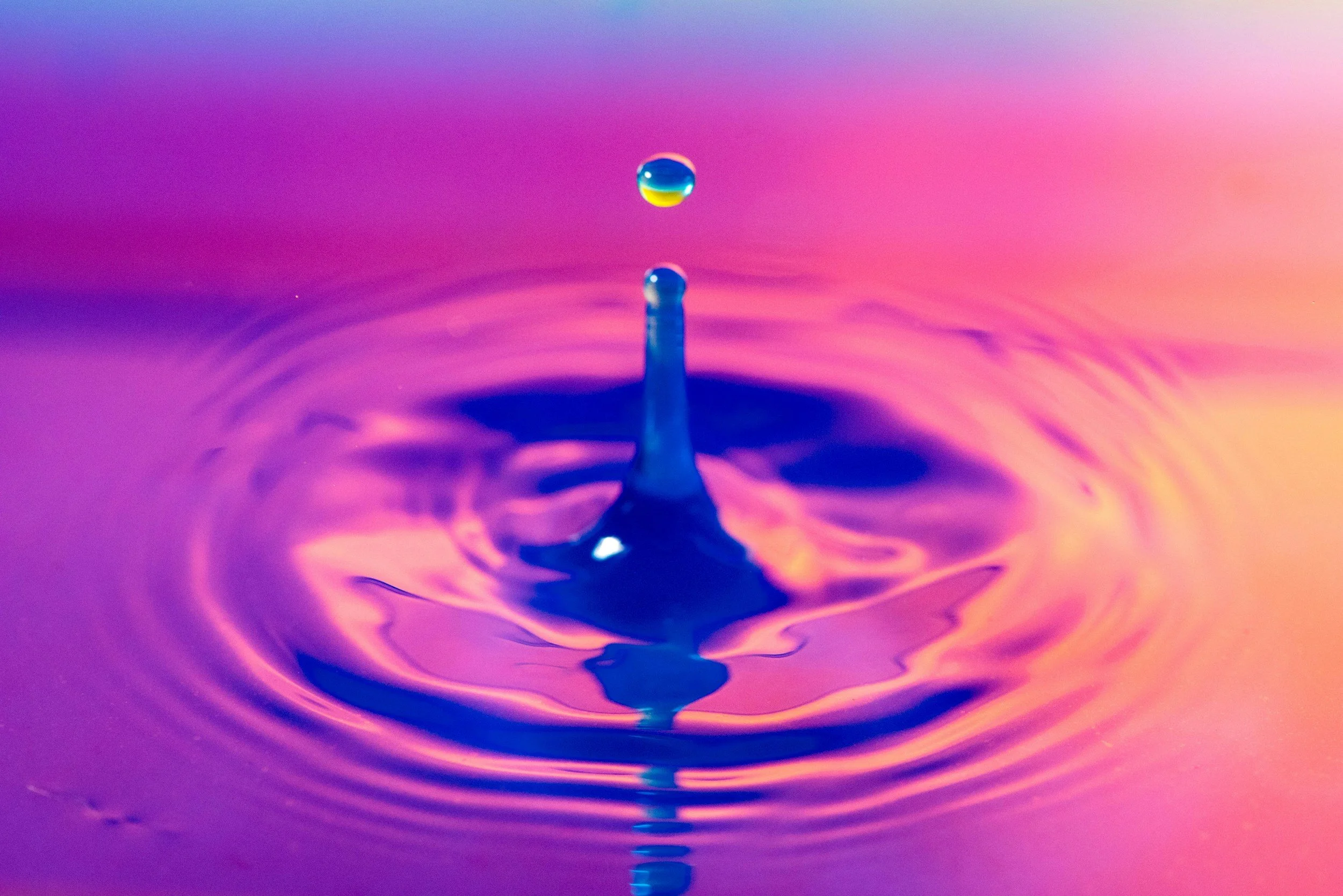 Gota de agua cayendo en agua con reflejos de colores rosa, azul y morado.