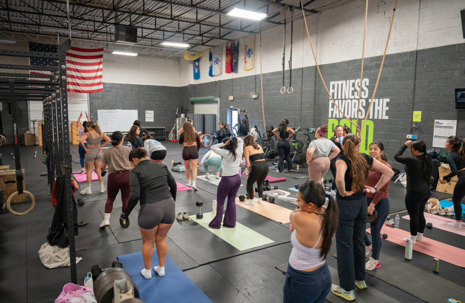 A group of women participating in a fitness class inside a gym, engaging in various exercises on yoga mats.