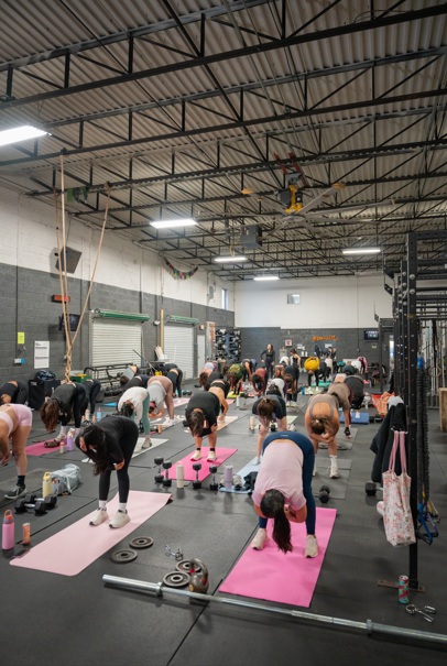 Group fitness class doing yoga or stretching on pink mats in a gym.