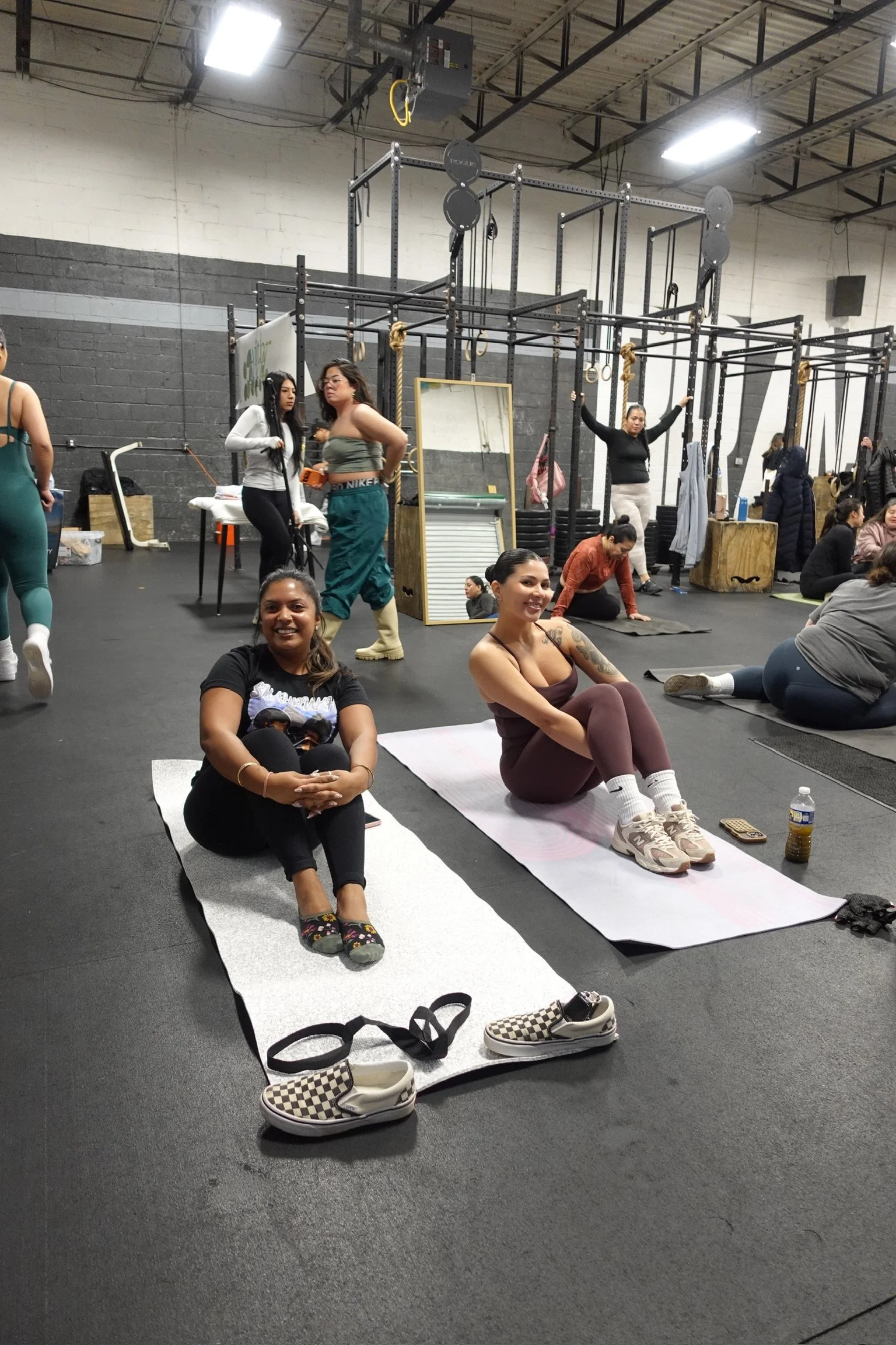 Women sitting on yoga mats in a gym, with other people working out in the background.