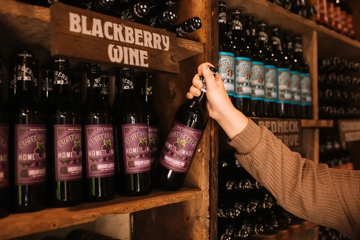 A modern building with a large glass window, surrounded by yellowish-green plants, set against a mountainous landscape with dry, grassy slopes and rocky peaks.