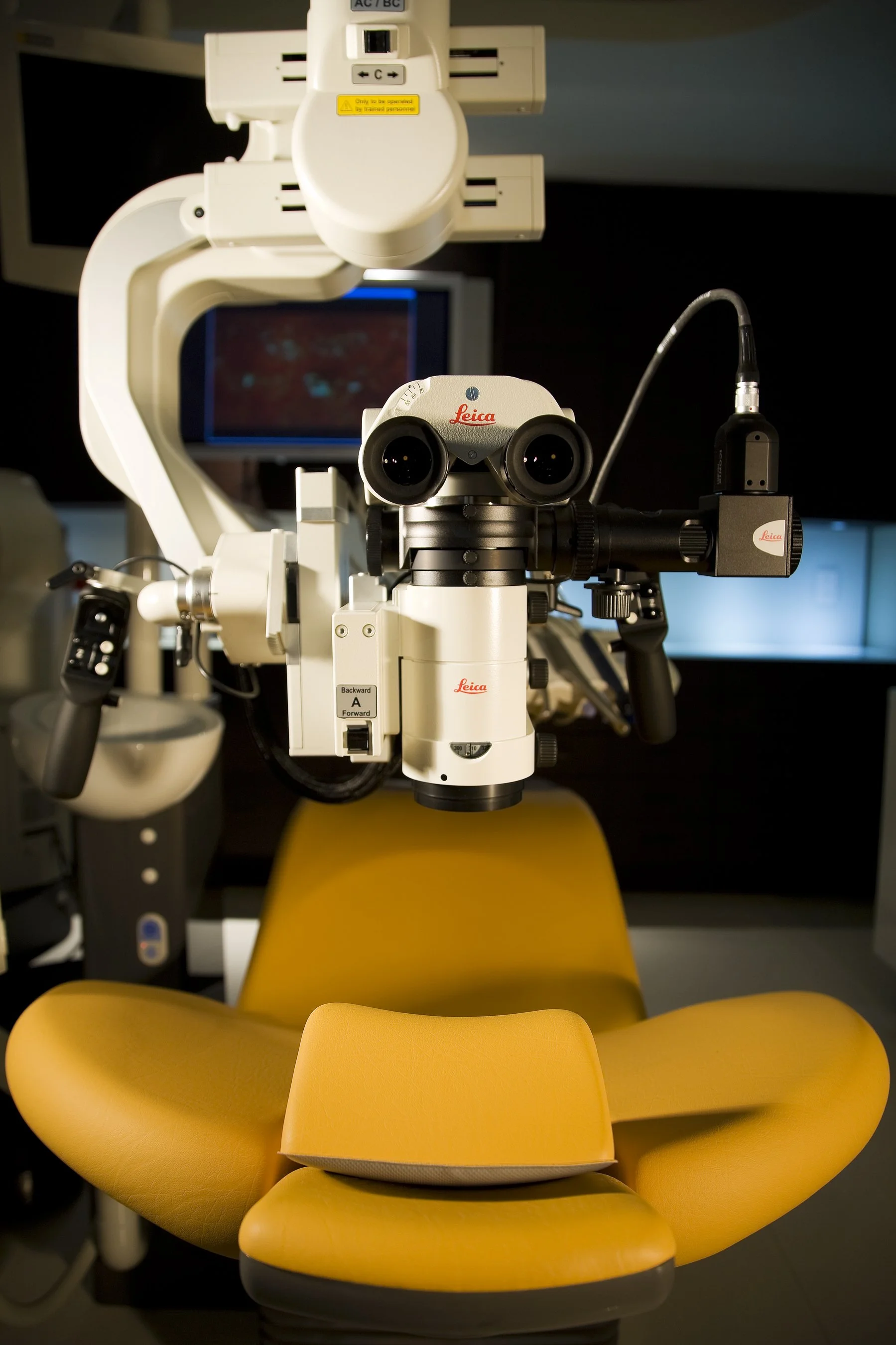 A Leica medical microscope positioned above a yellow examination chair in a medical room.