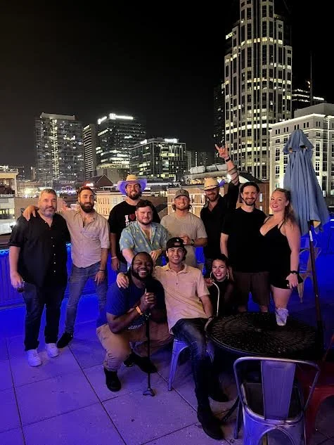 Group of people enjoying a night out on a rooftop with city skyline in the background.