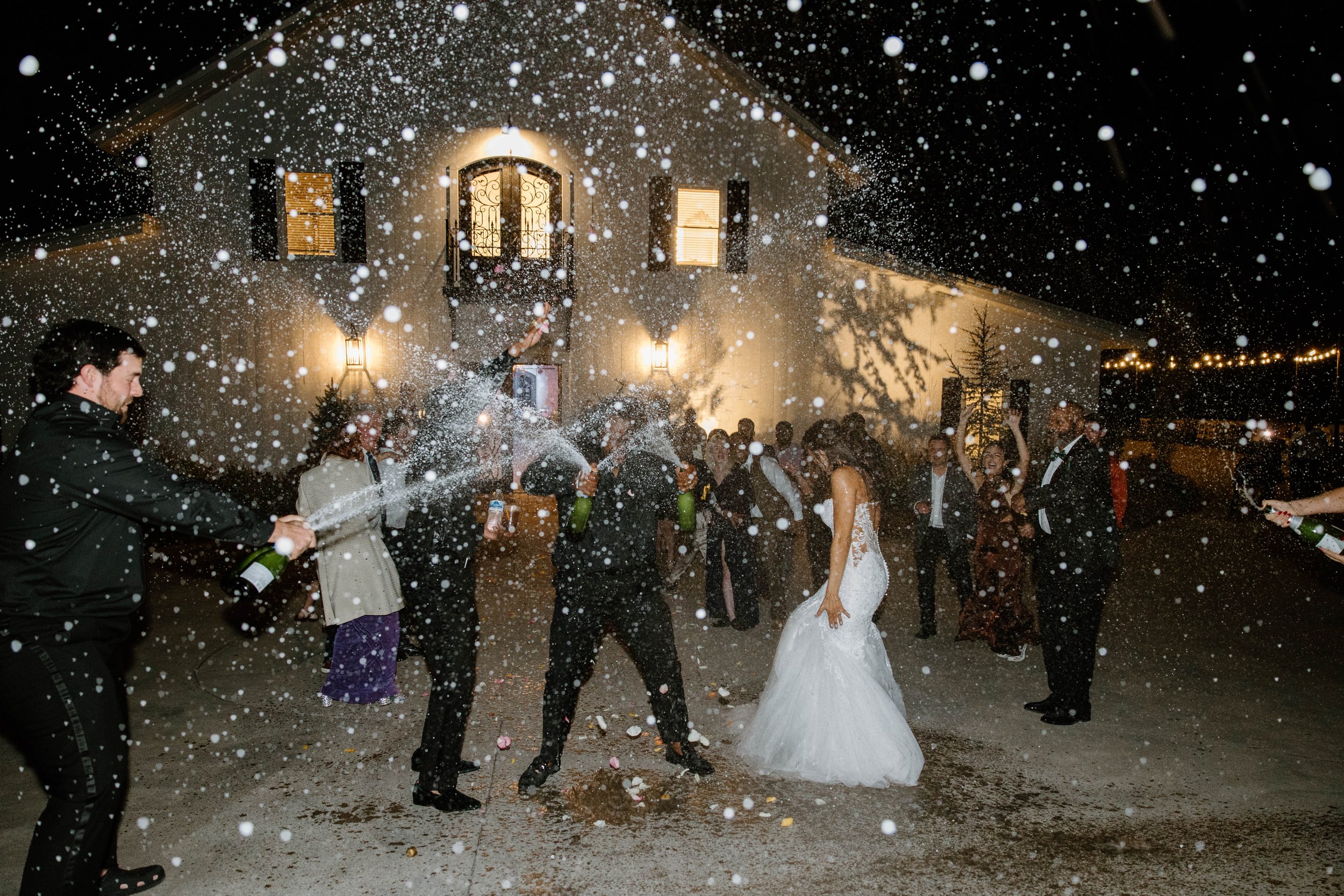 People celebrating a wedding outside at night with champagne and snow falling.