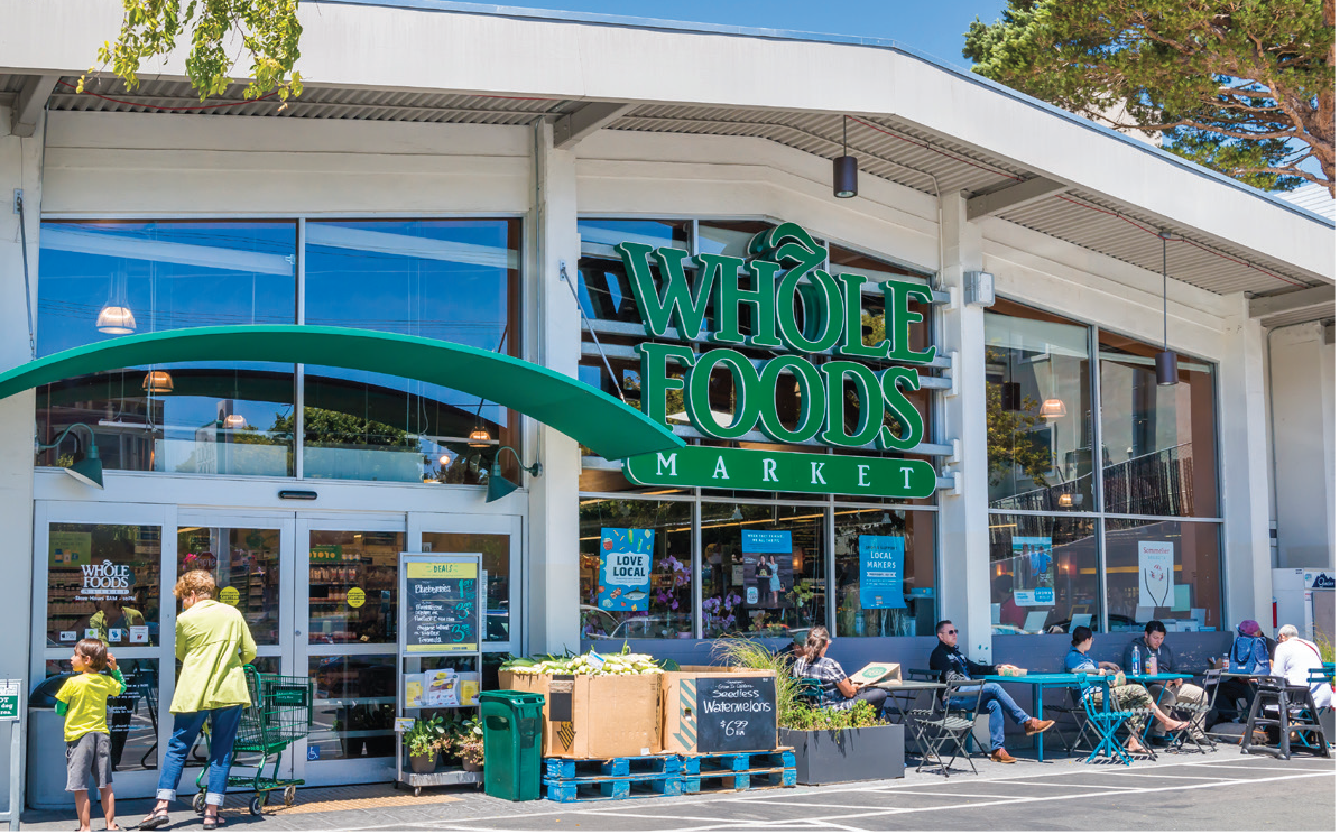 Exterior of Whole Foods Market with people sitting outside and shopping.