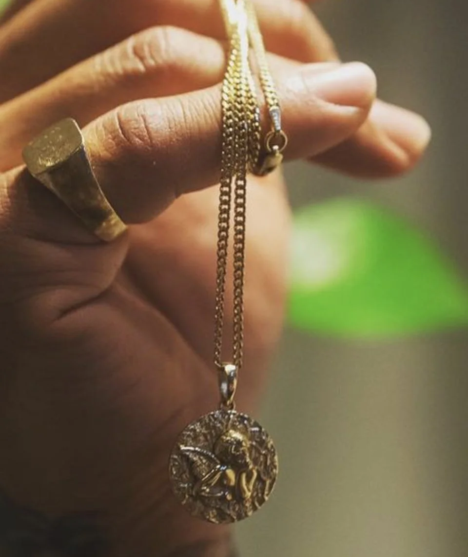 Close-up of a hand holding a gold chain necklace with a round pendant featuring a bee design.