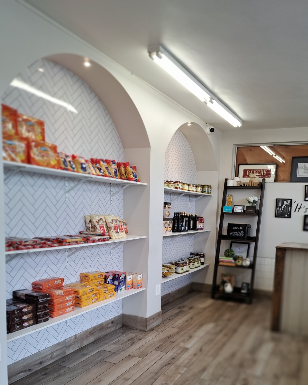 Shelf with snacks and jars in a bakery or cafe shop, wooden floor, decorative wall, black shelving unit with framed pictures and decor.
