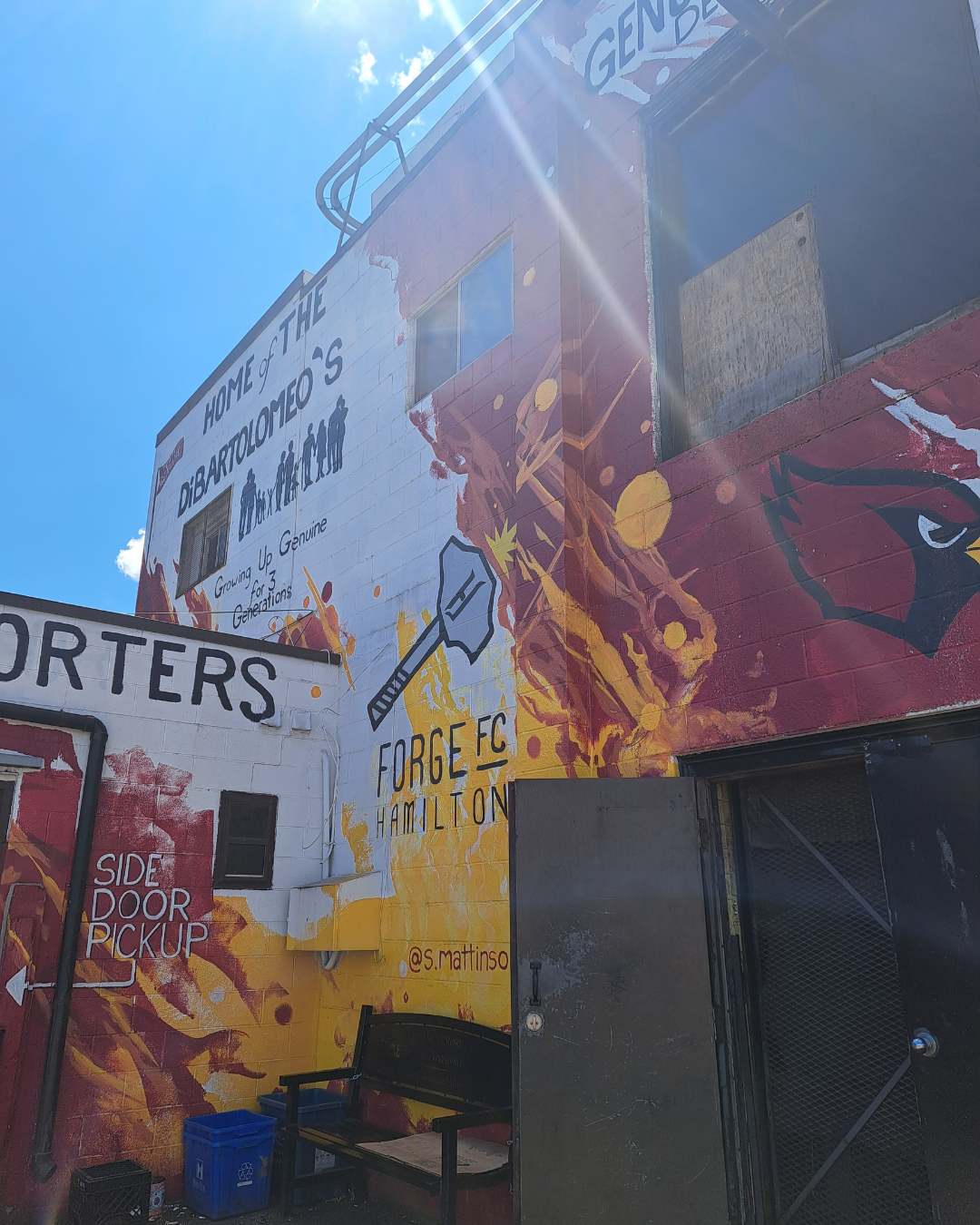 Colourful mural at Genuine Bakery and side door pickup, and a bench below.