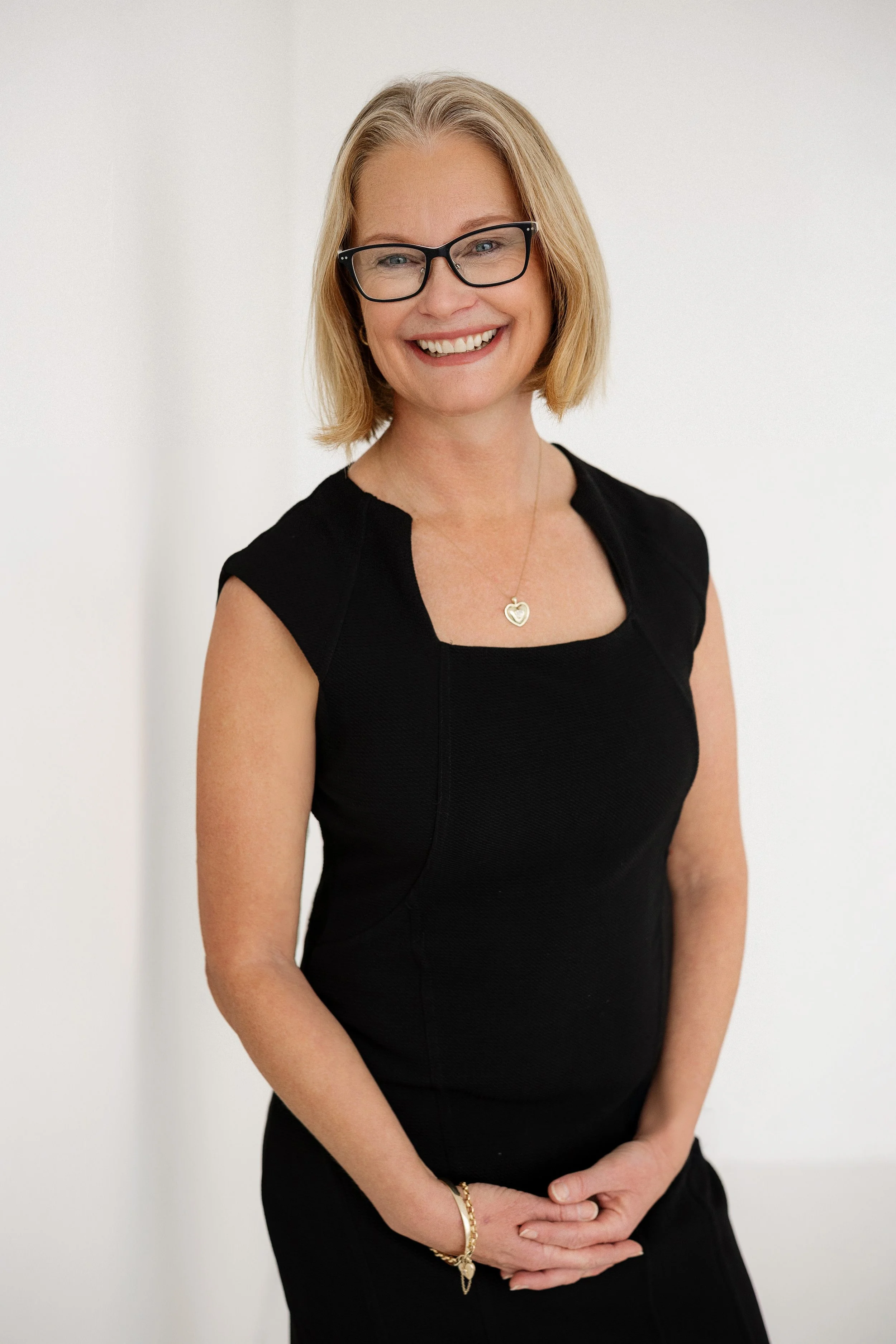 Health Coach Vicki Carne - a woman with blonde hair, glasses, and a black dress smiling and standing against a white background.