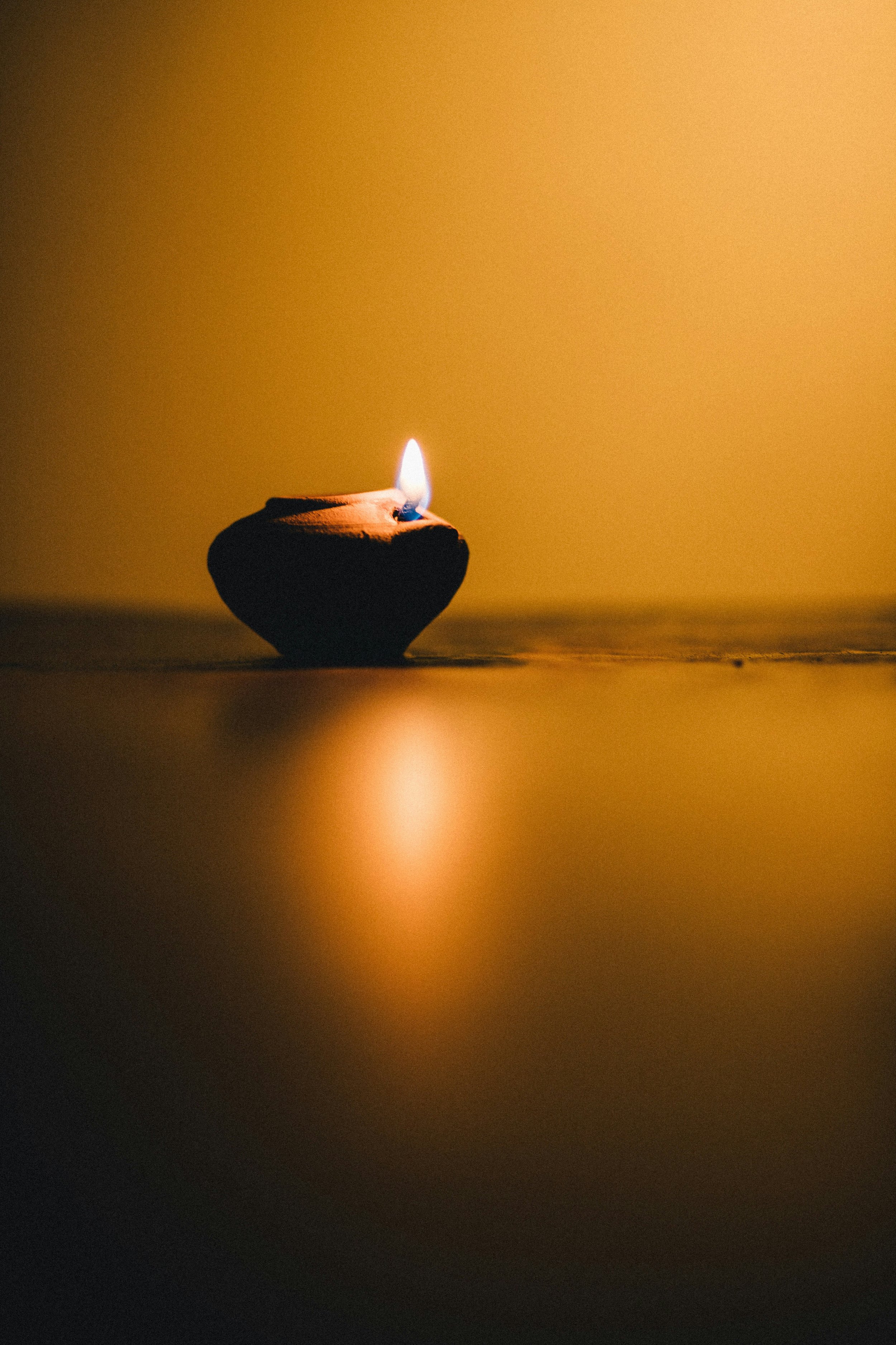 A small clay oil lamp with a lit flame on a smooth surface, casting a warm glow.