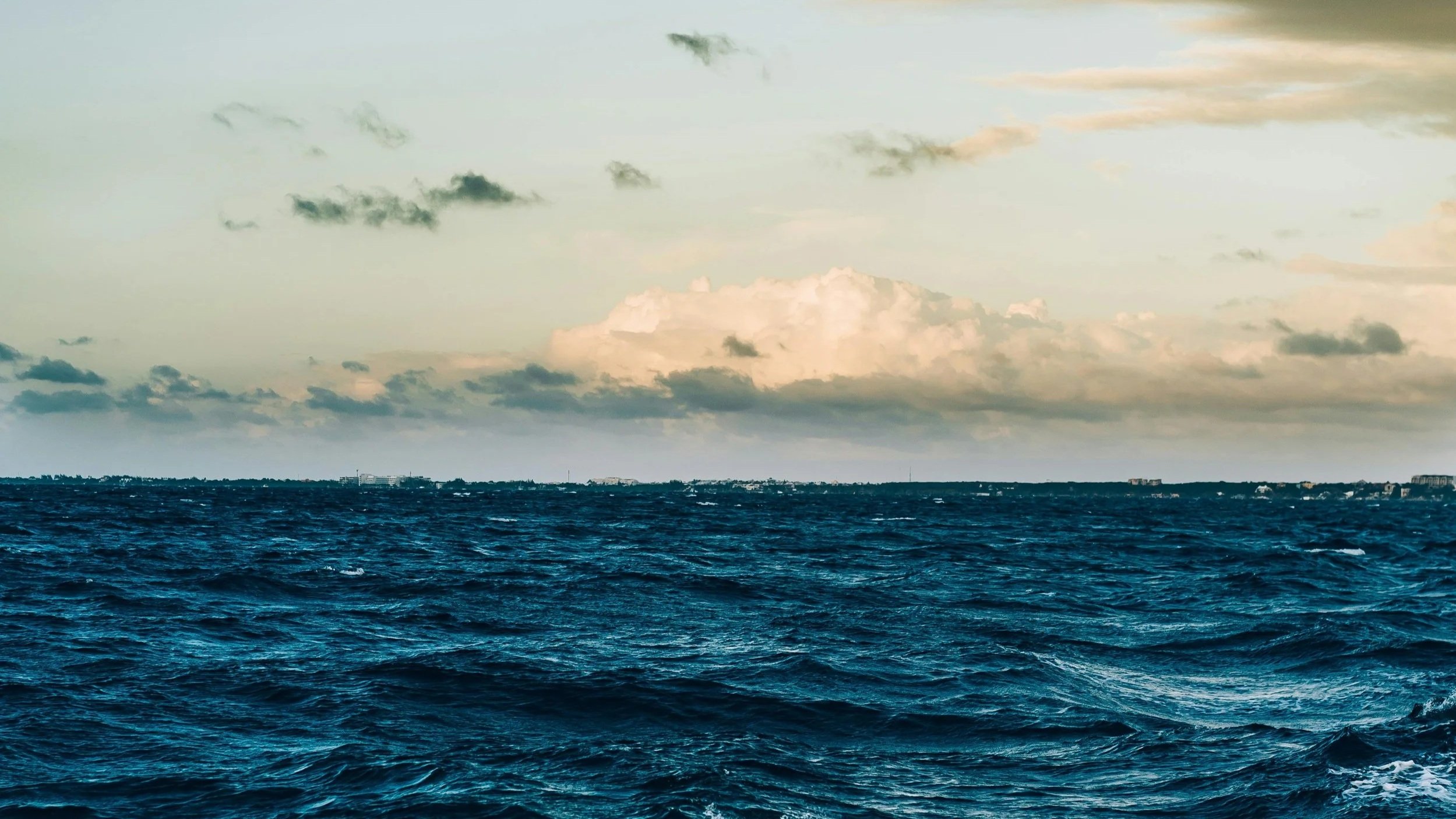 Blick auf eine stürmische Meeresoberfläche bei Sonnenuntergang mit Wolken am Himmel