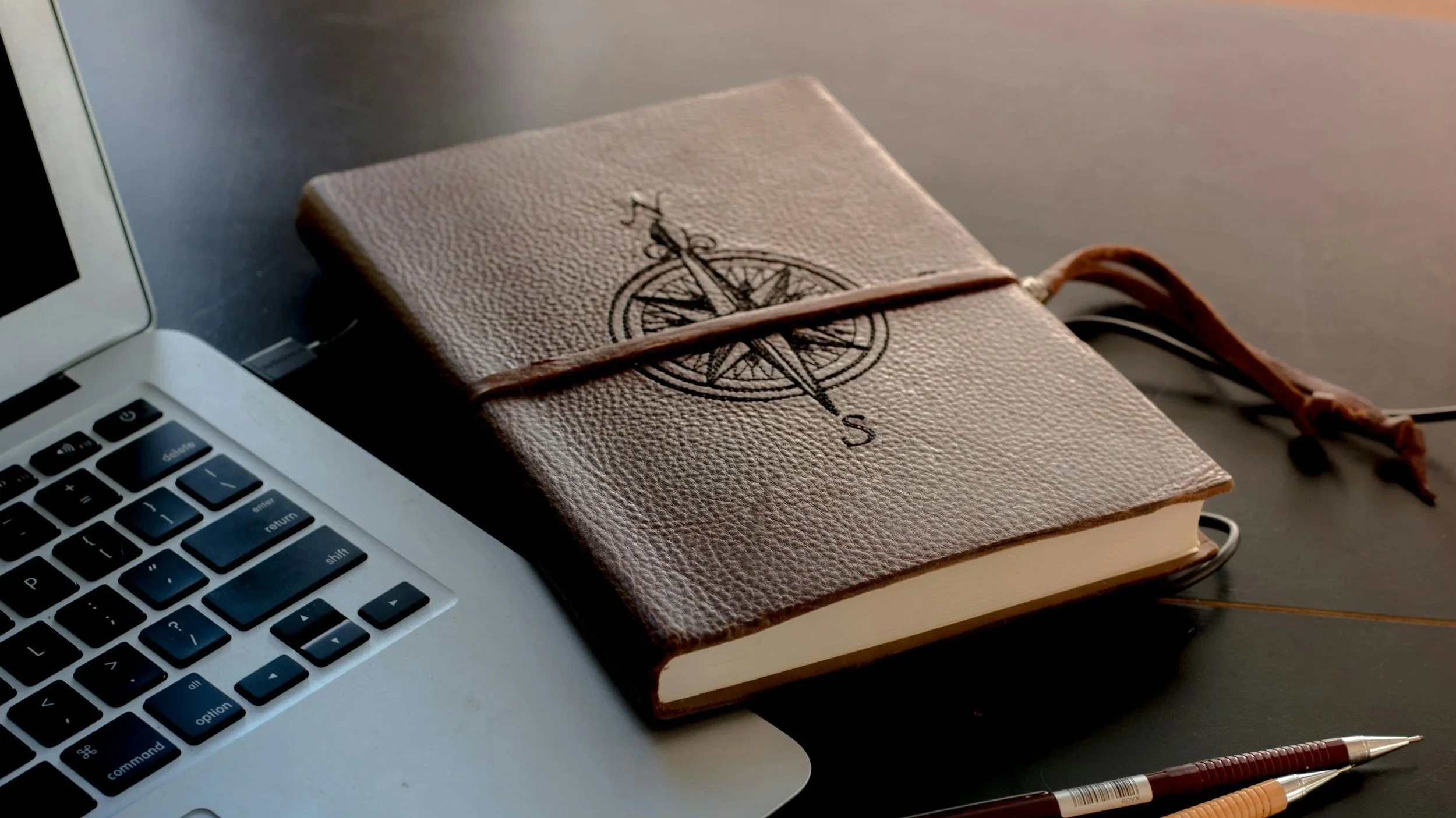 leatherbound notebook with compass stitched next to computer