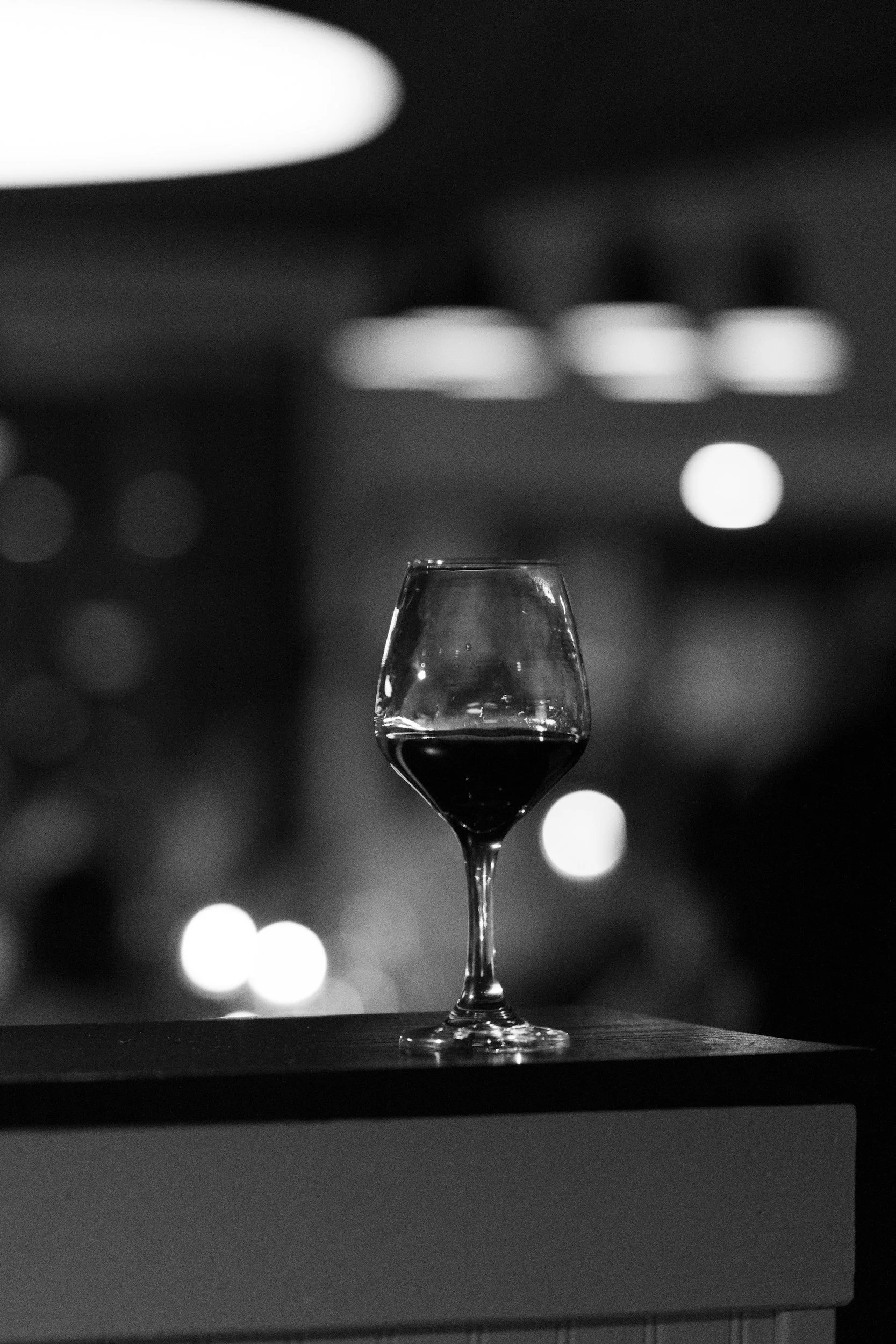 A glass of red wine on a table in a dimly lit setting with blurry lights in the background