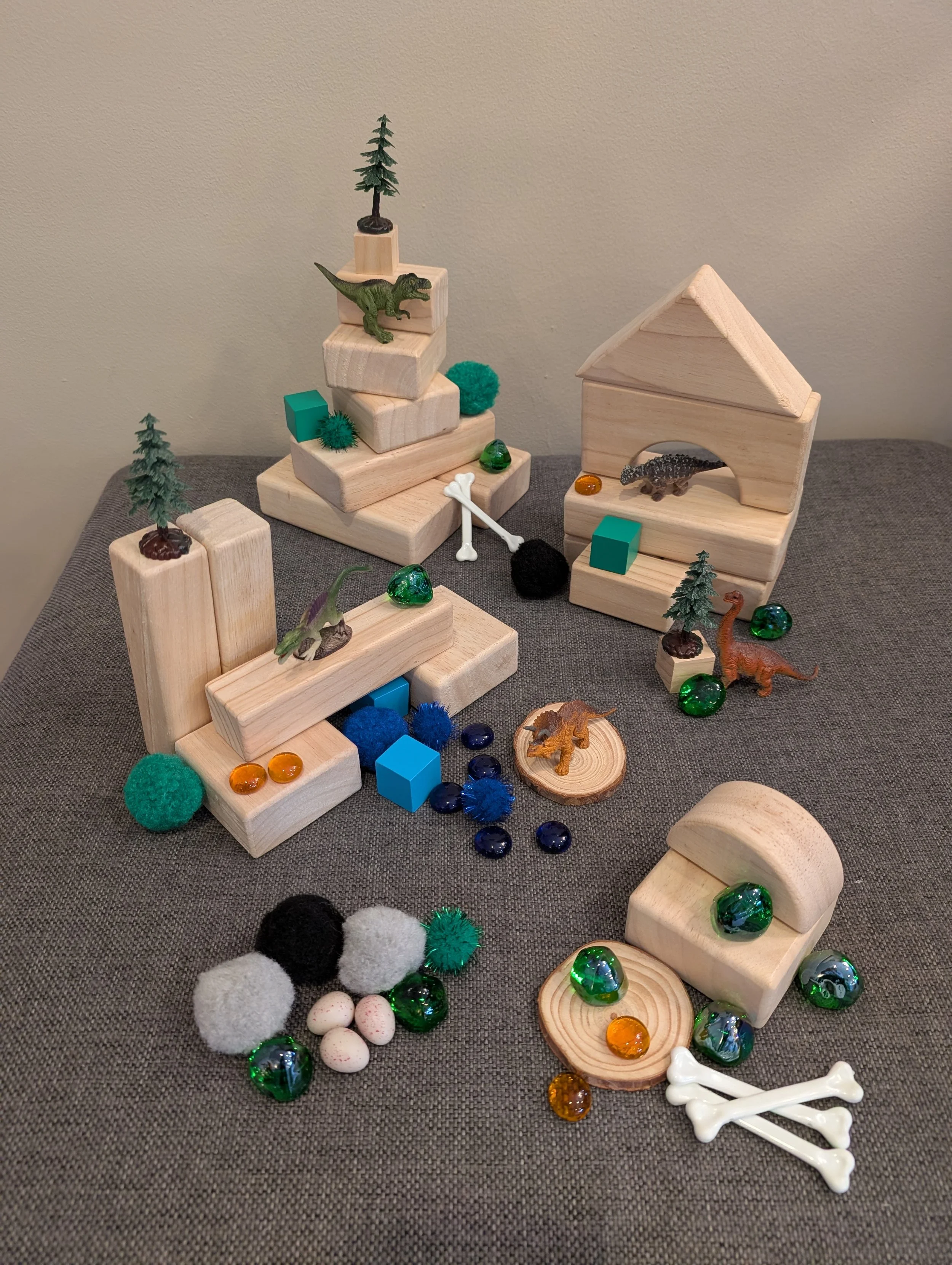 Creative, open-ended play scene built with Play Sparks Dinosaur Box loose parts arranged with wooden blocks; imaginative dino world building play for kids ages 4 to 8