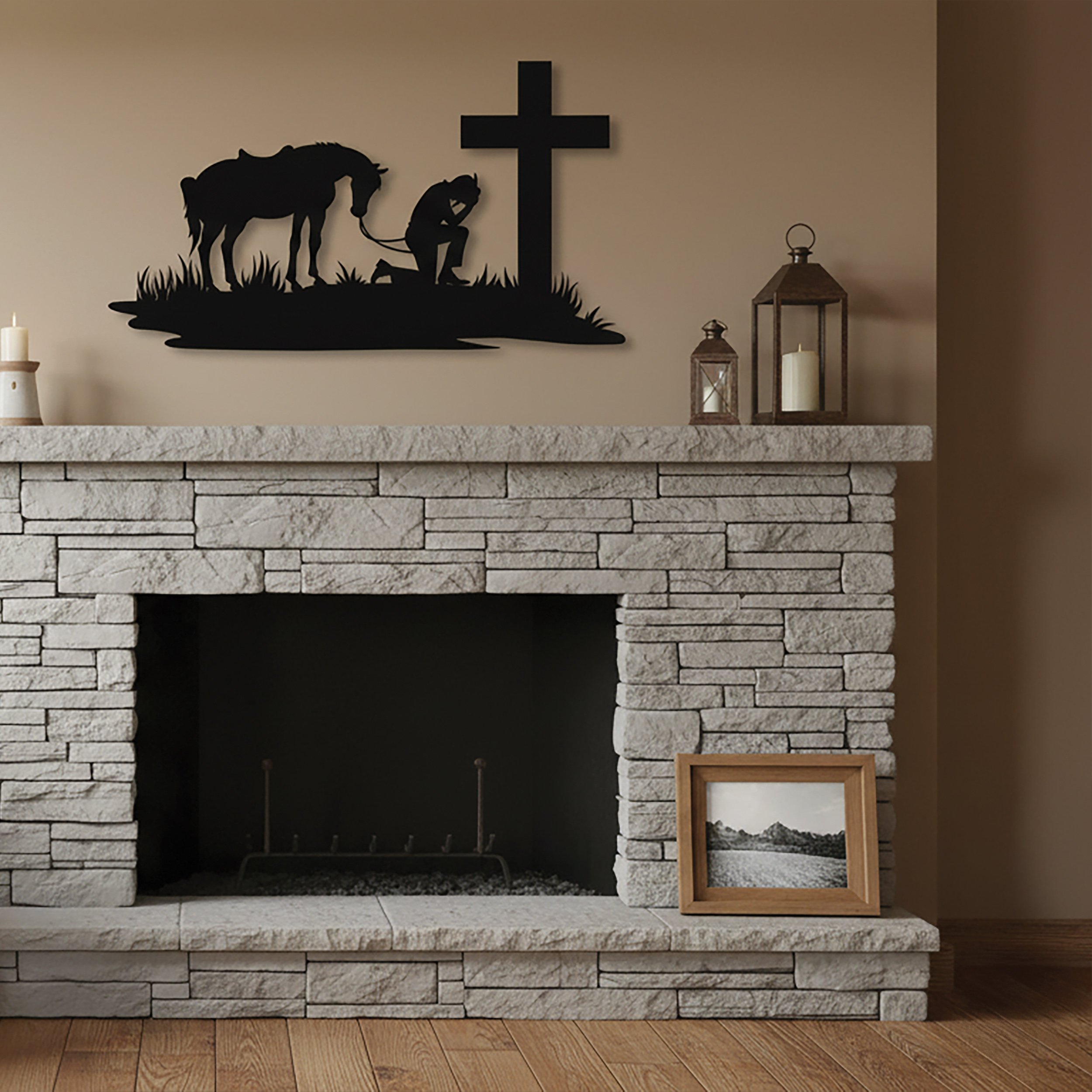 Large black metal wall art of a serene scene depicting a man kneeling in front of a large cross, his horse standing behind him, with the reins draped along the ground, hanging over a stone fireplace, in a modern neutral living room.