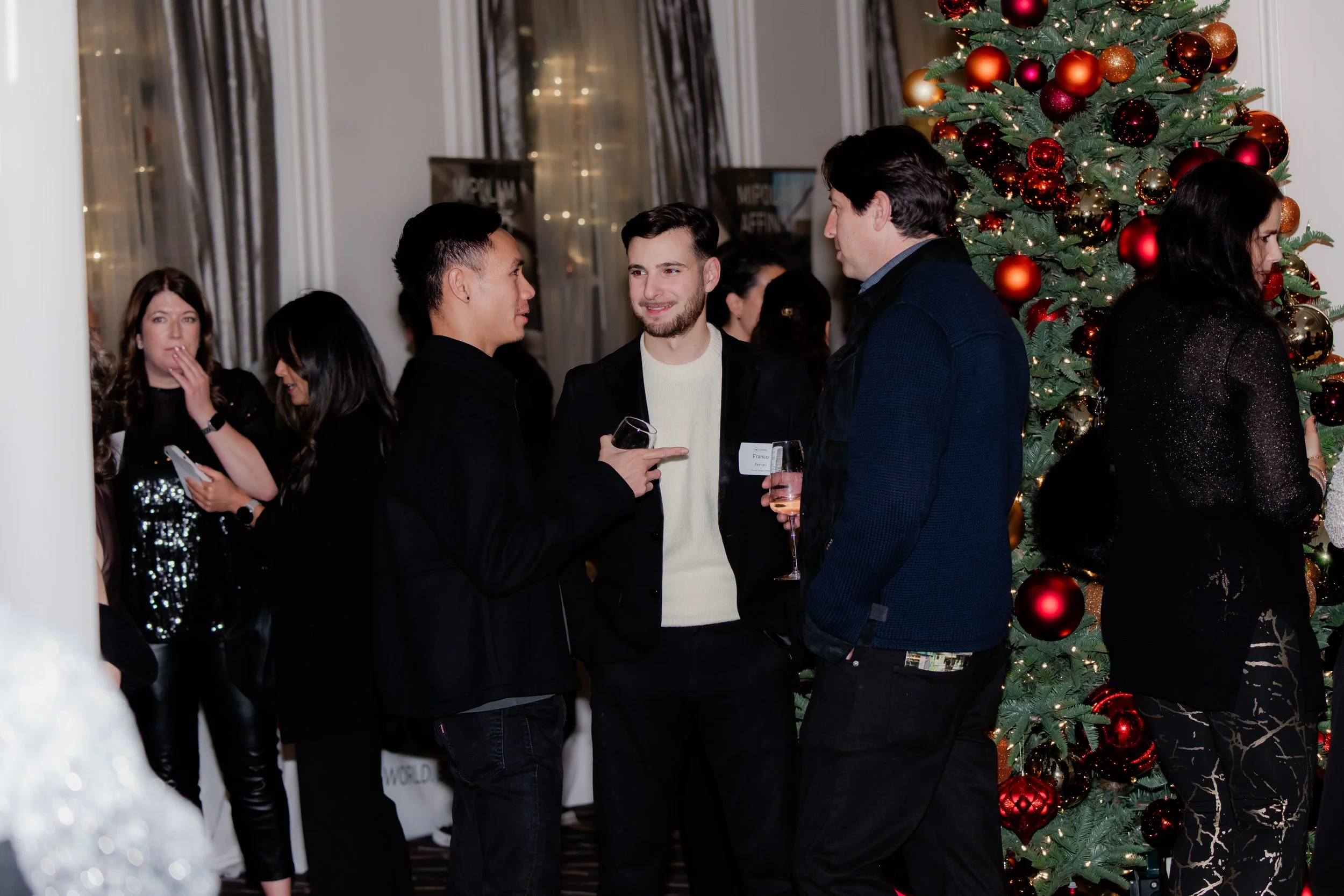 People at a holiday party socializing near a decorated Christmas tree.