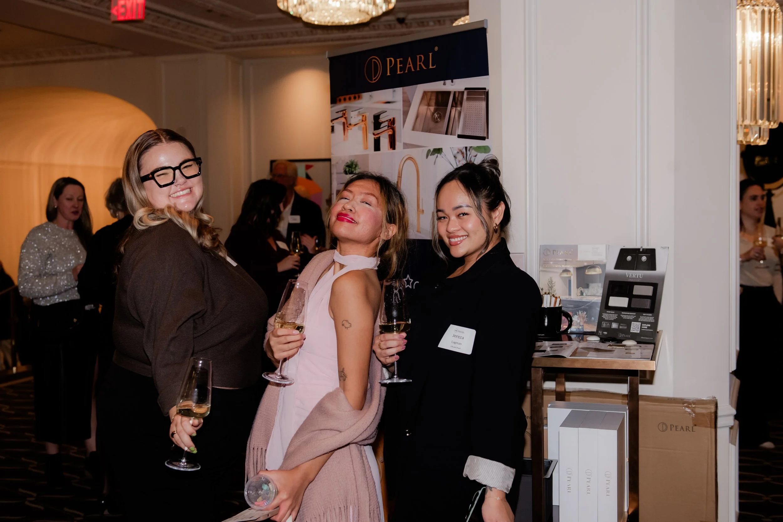 Three women smiling and holding glasses of champagne at a social event.