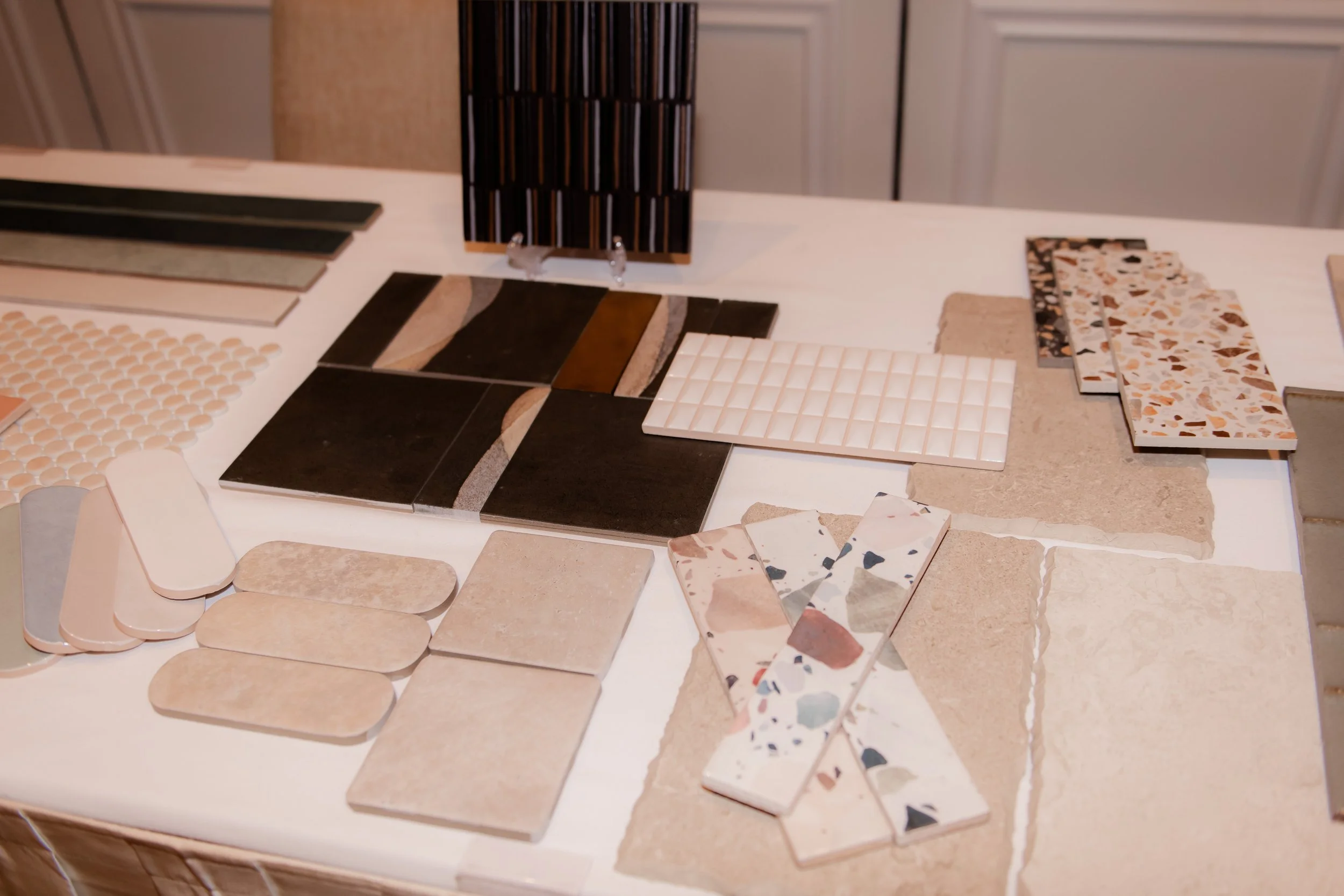 Various ceramic tile samples in different colors, sizes, and patterns laid out on a table.