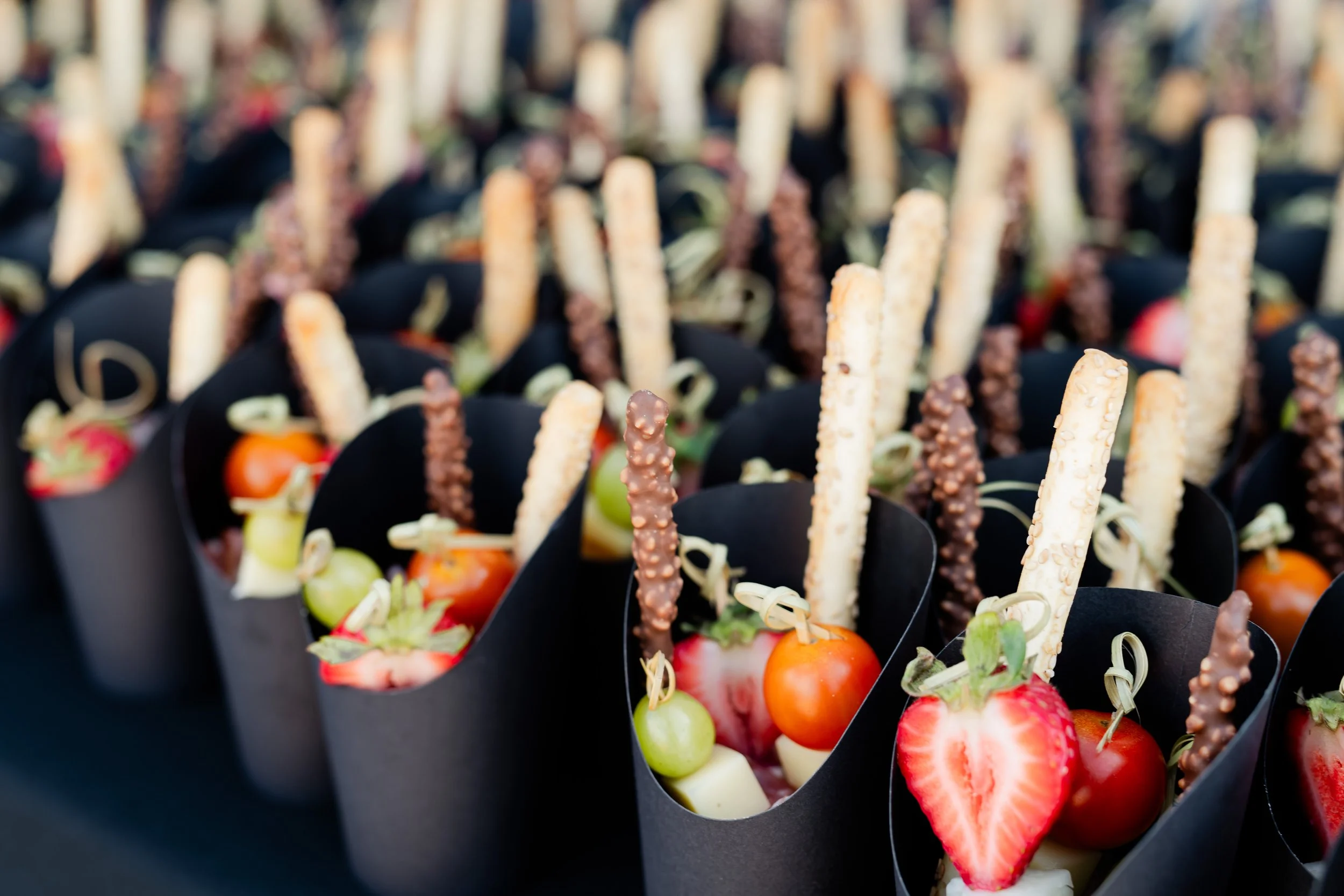 Individual dessert cups with strawberries, green grapes, white chocolate, and crispy biscuit sticks, garnished with chocolate-covered pretzel sticks.