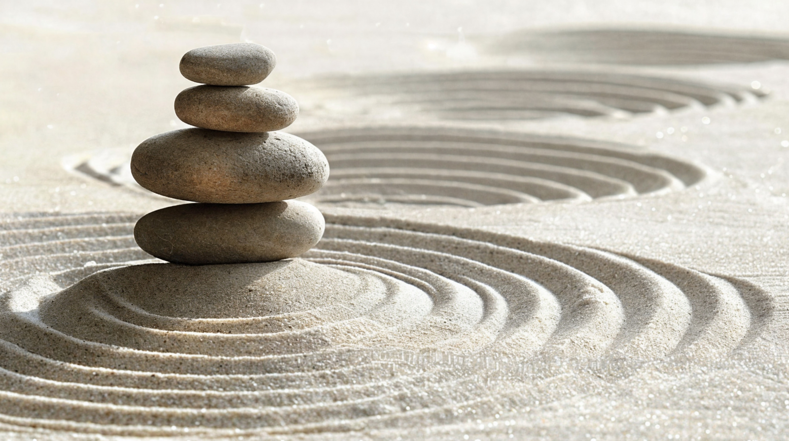 Stacked smooth stones on sand with concentric raked sand patterns at a Zen garden.