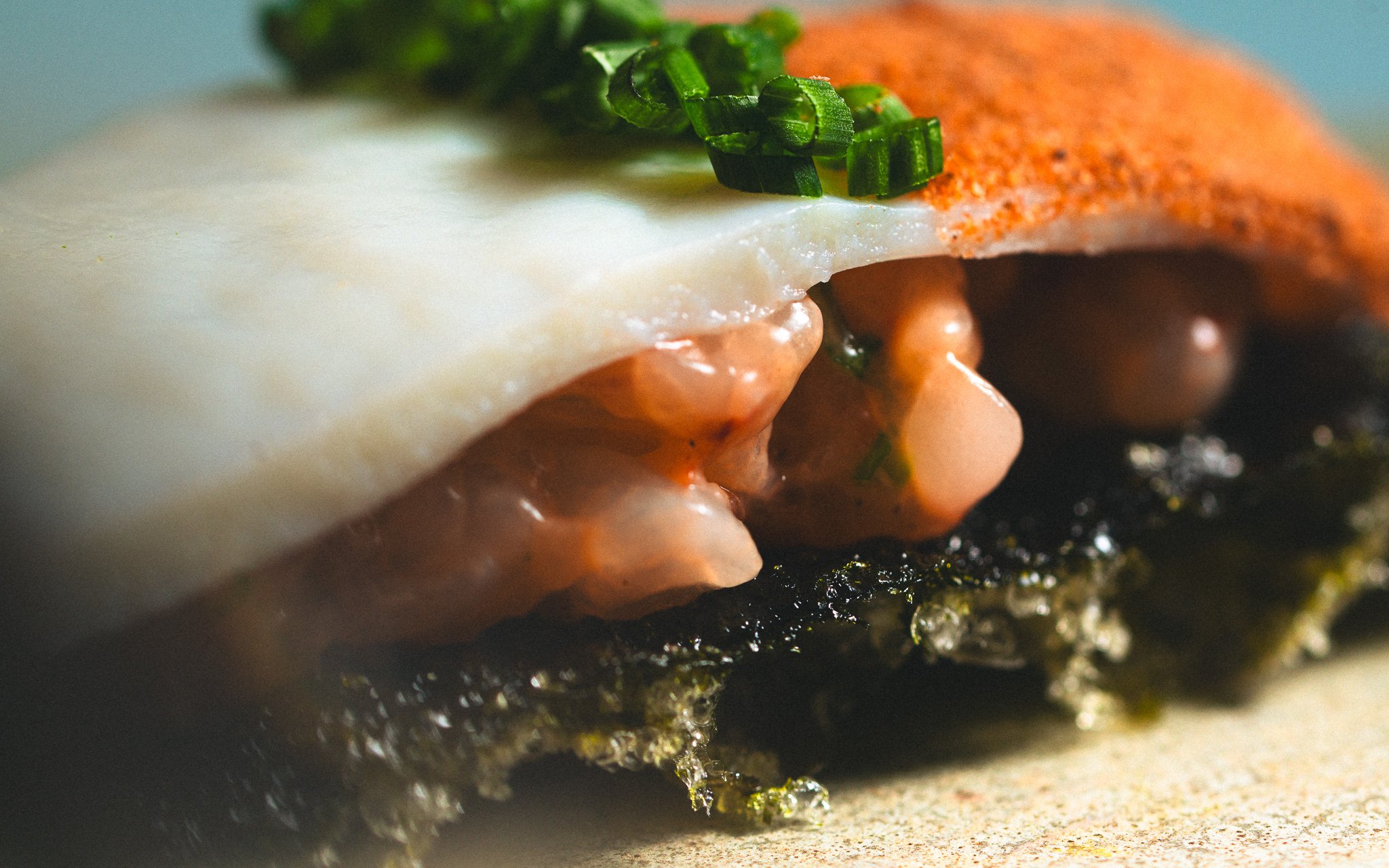 Close-up of eggs benedict with poached eggs, hollandaise sauce, and chopped green herbs on an English muffin, with a side of smoked salmon and a dusting of paprika.