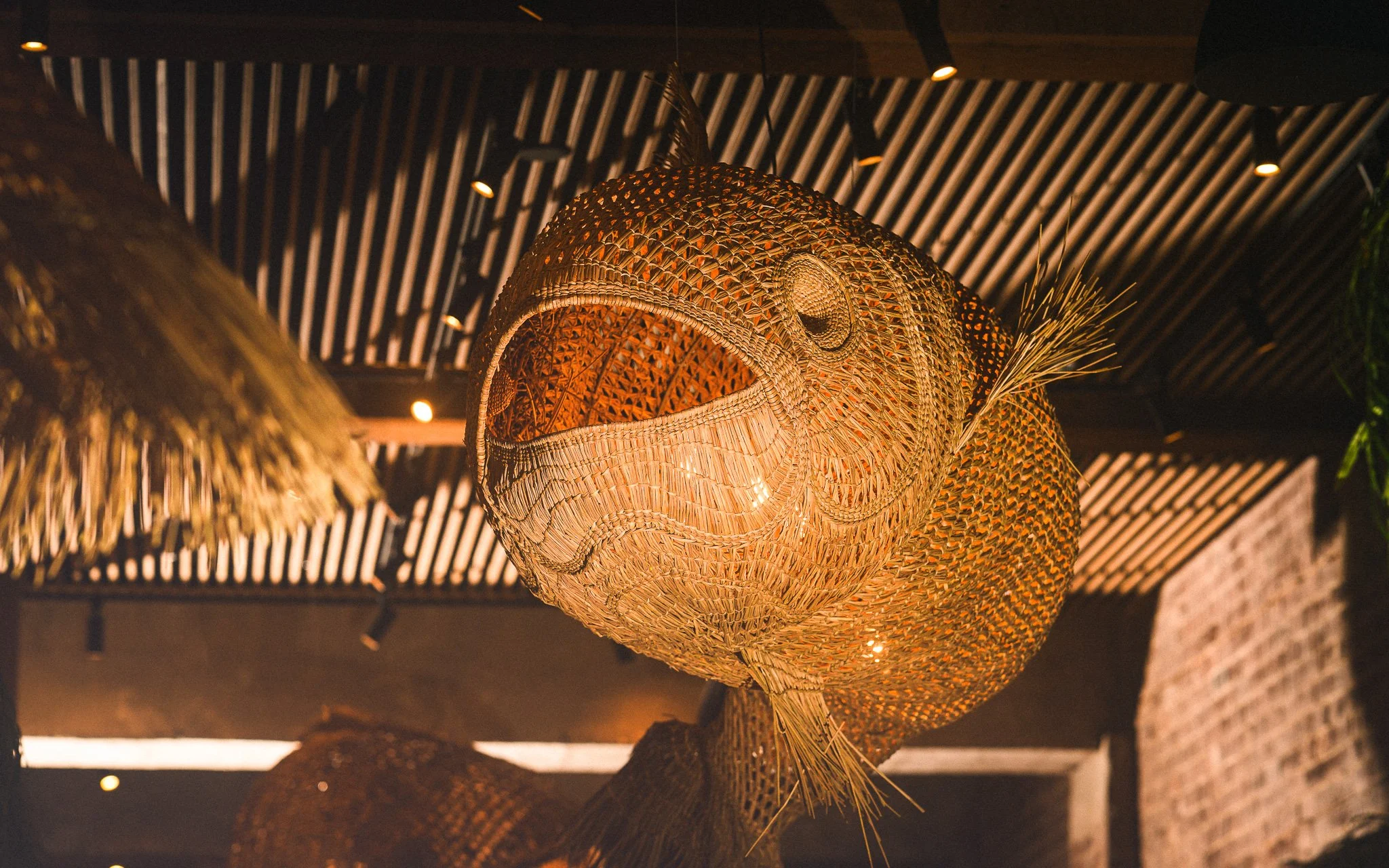 A woven rattan pendant light fixture hanging from the ceiling with warm lighting, part of a rustic or tropical interior decor.