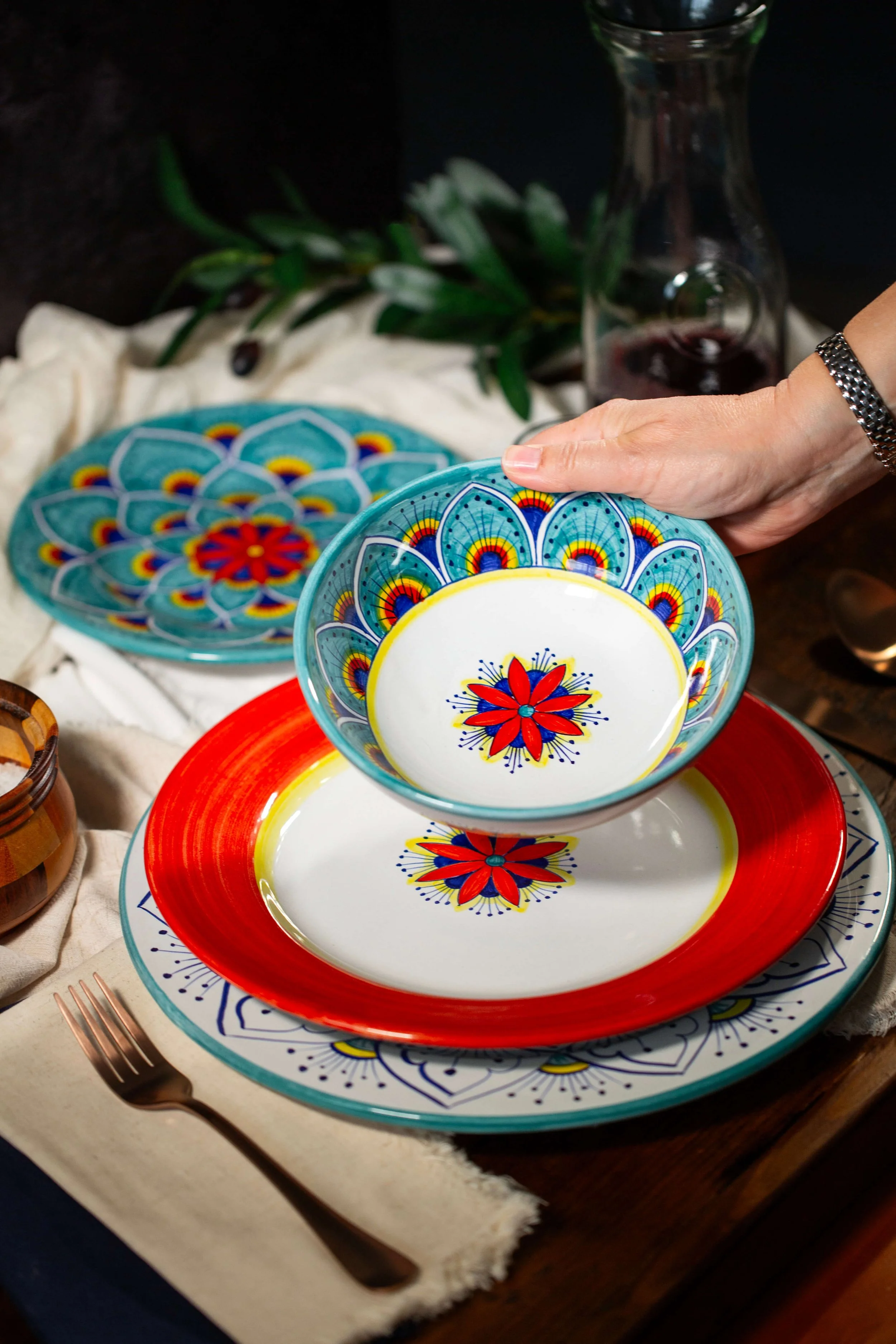 Hand placing Intreccio Italian ceramic bowl on layered red and teal place setting