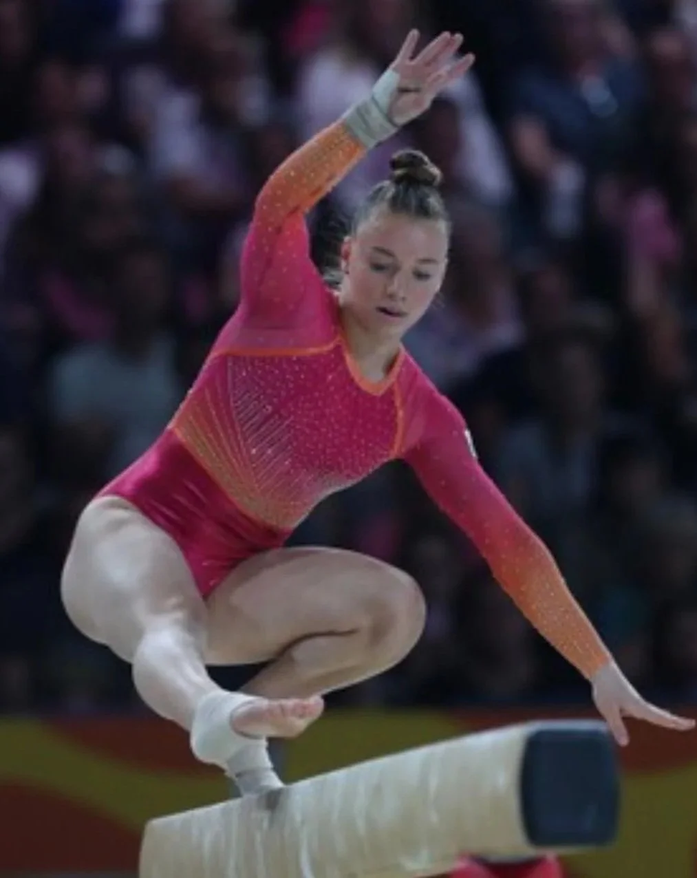 Young female gymnast in a pink and orange leotard balancing on a balance beam during a competition.