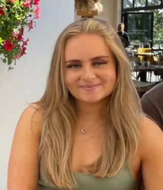 A young woman with long blonde hair smiling at a restaurant or café.