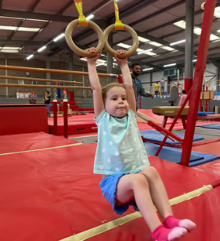 Young girl with blond hair hanging from gymnastic rings at an indoor playground.