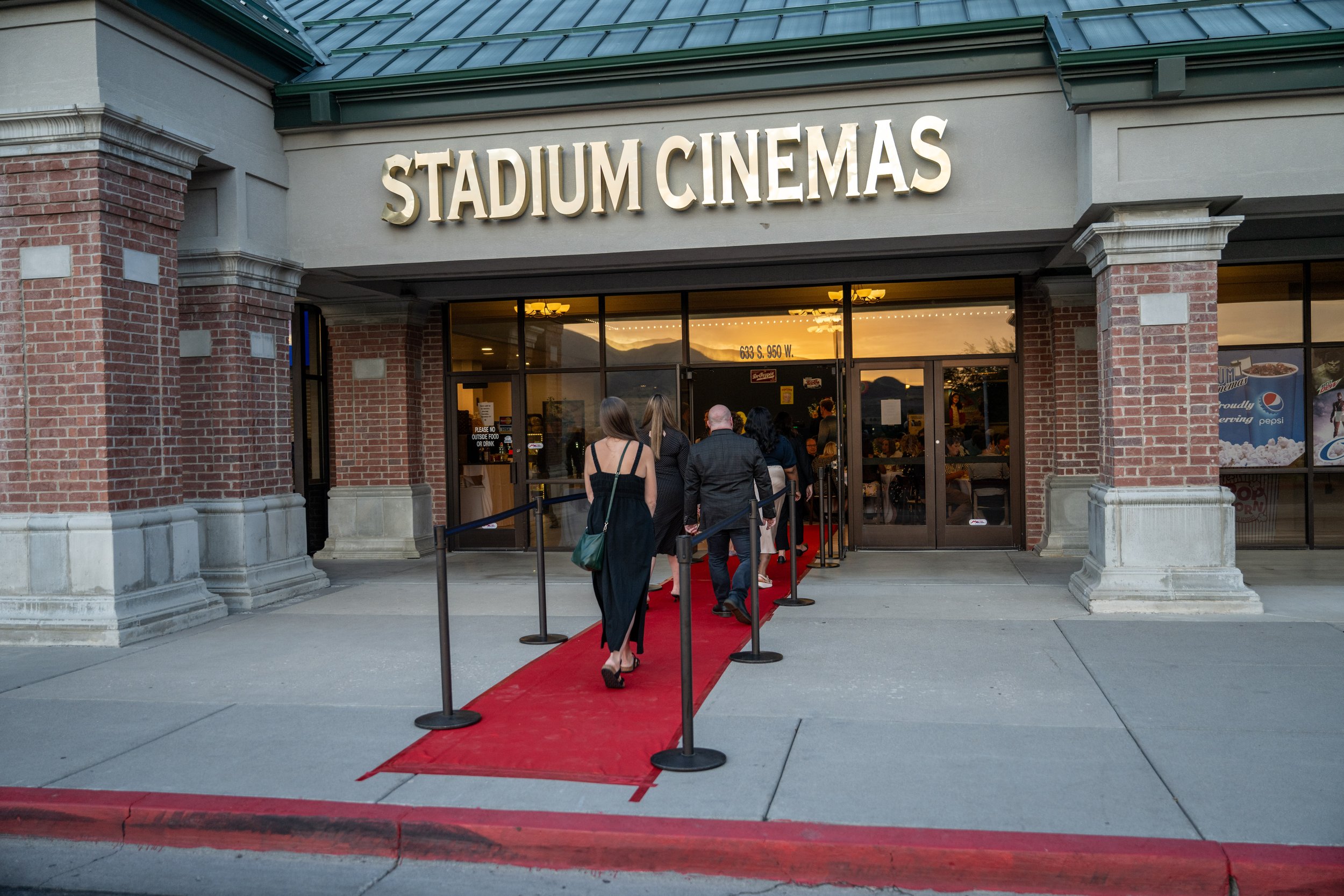 People walking up a red carpet into Stadium Cinemas theater during the evening.