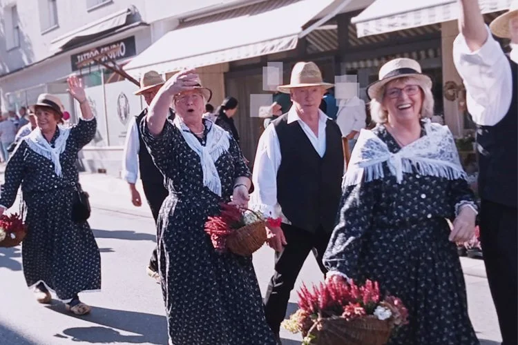 Mitglieder des Heimatvereins Augustdorf nehmen an einem Umzug teil. Sie tragen traditionelle Trachten mit weißen Punkten, weißen Halstücher und Hüte. Einige tragen Körbe mit Blumen.