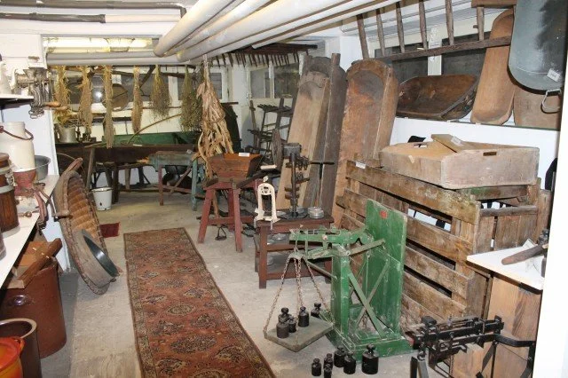 Altes handwerkliches Werkzeug und Geräte in einer Werkstatt, inklusive Waage, Holzschlitten, Pressen und Werkbänke