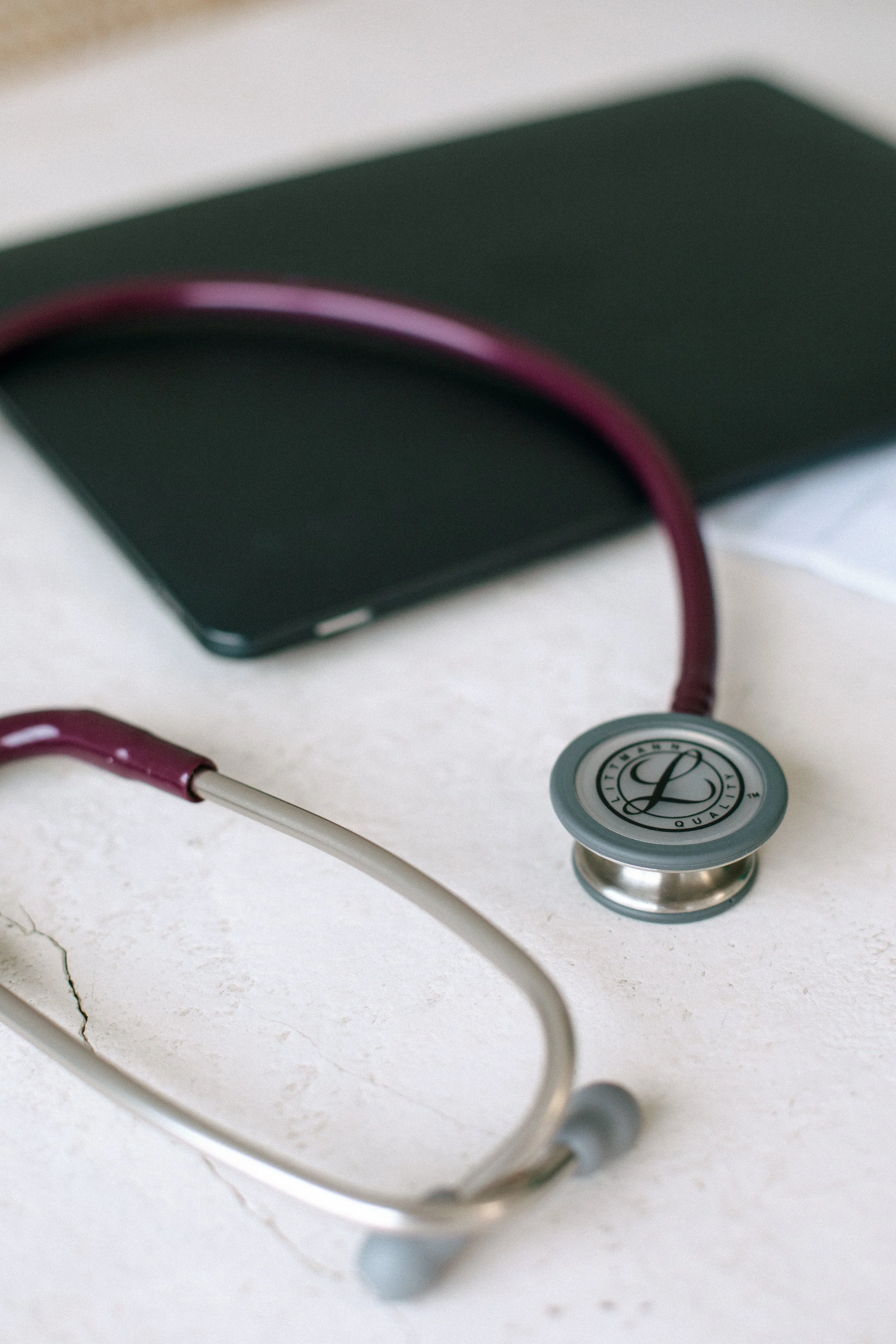 Close-up of a stethoscope resting on a white surface with visible cracks, and part of a dark-colored object in the background.