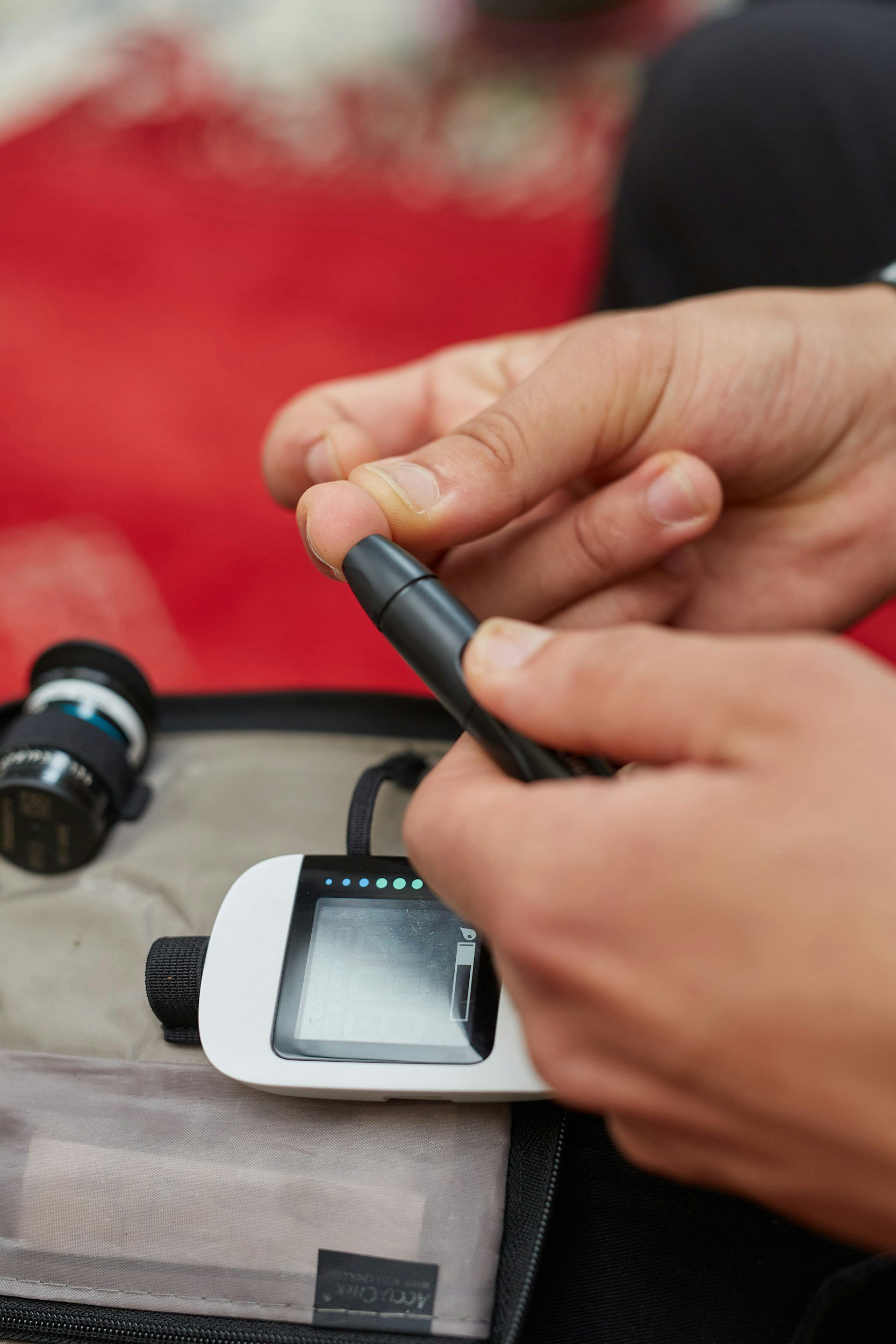 Close-up of a hand adjusting the settings on a device with a digital screen, with a blurred background showing a red object and a black object.