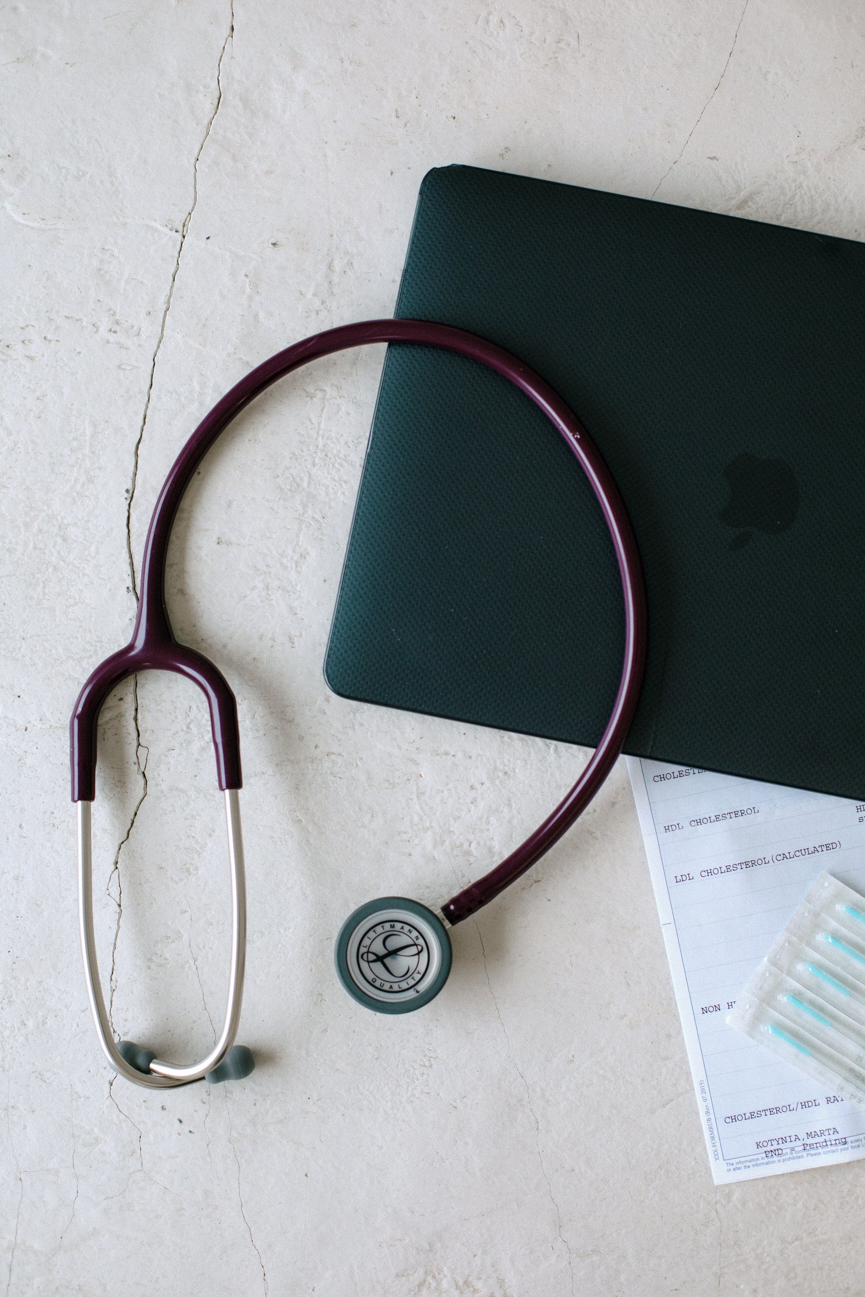 A stethoscope resting on a table next to a dark green notebook and a partial sheet of medical notes.