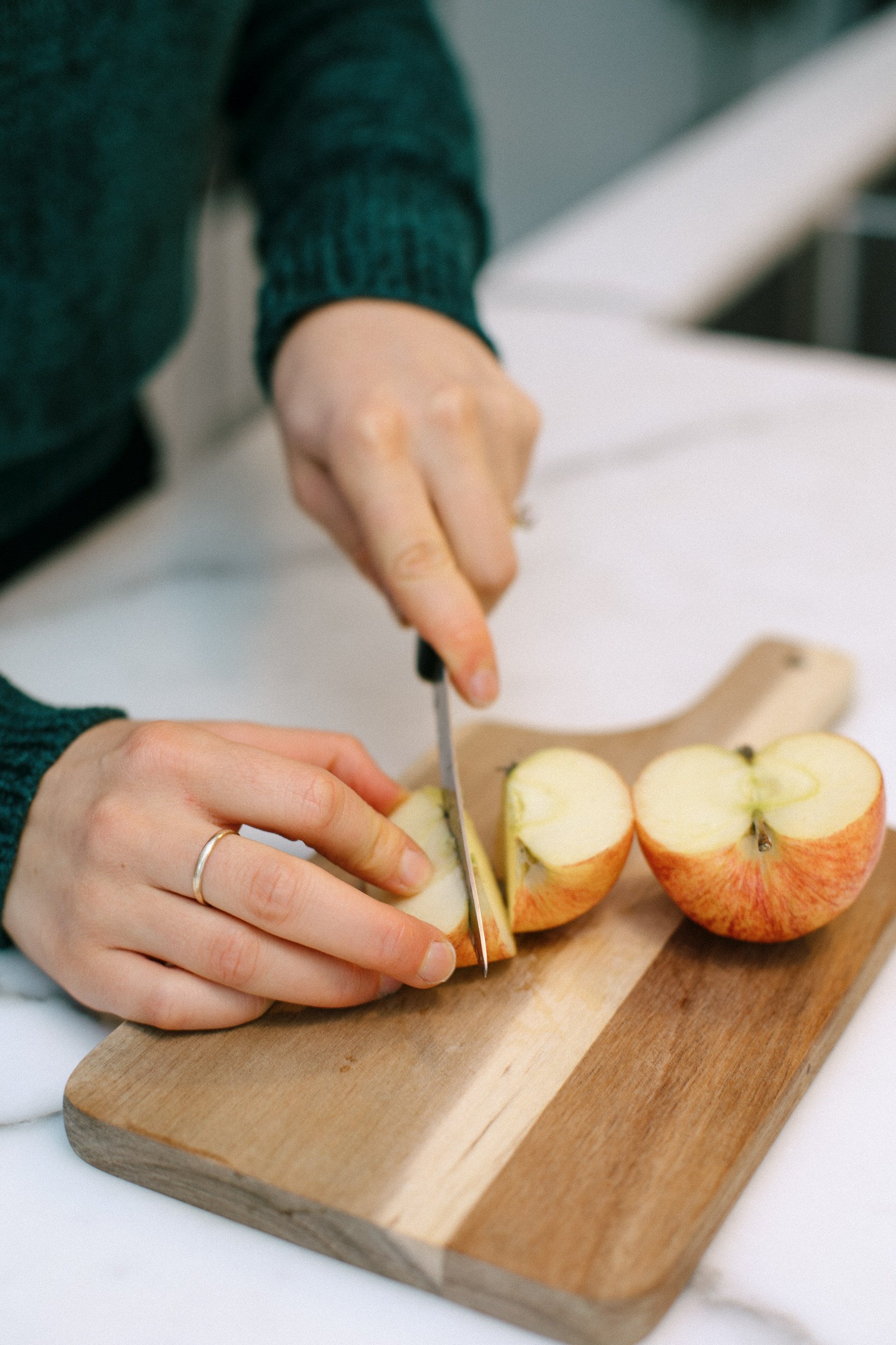 Person slicing an apple on a wooden cutting board.