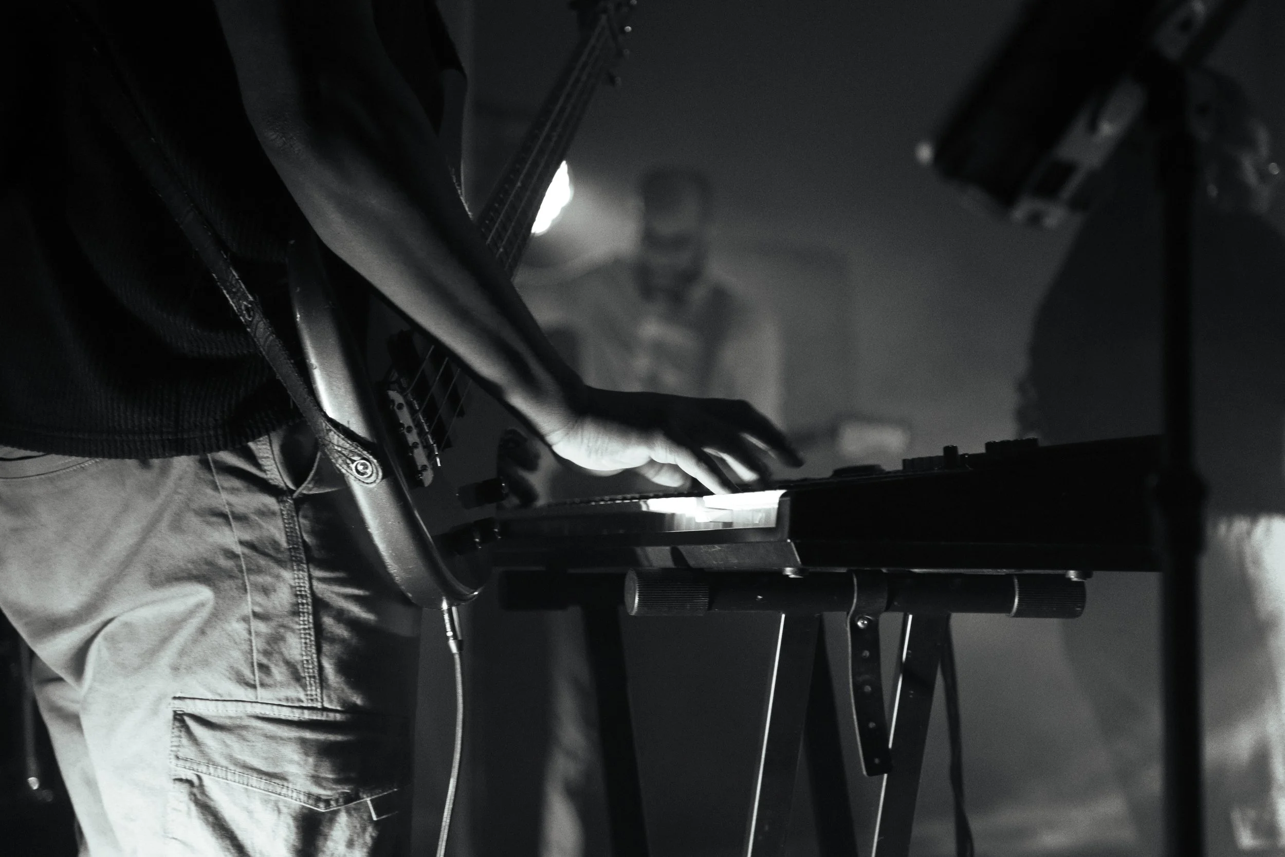 Person playing a black grand piano in a dark setting, with focus on the hands on the keyboard.