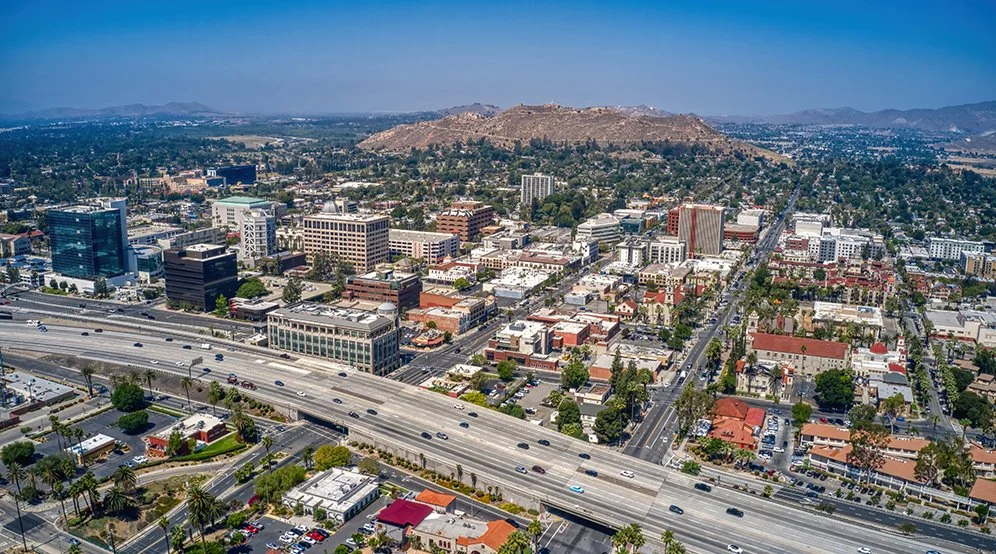 Aerial view of a cityscape with a highway, various buildings, and hills in the background.
