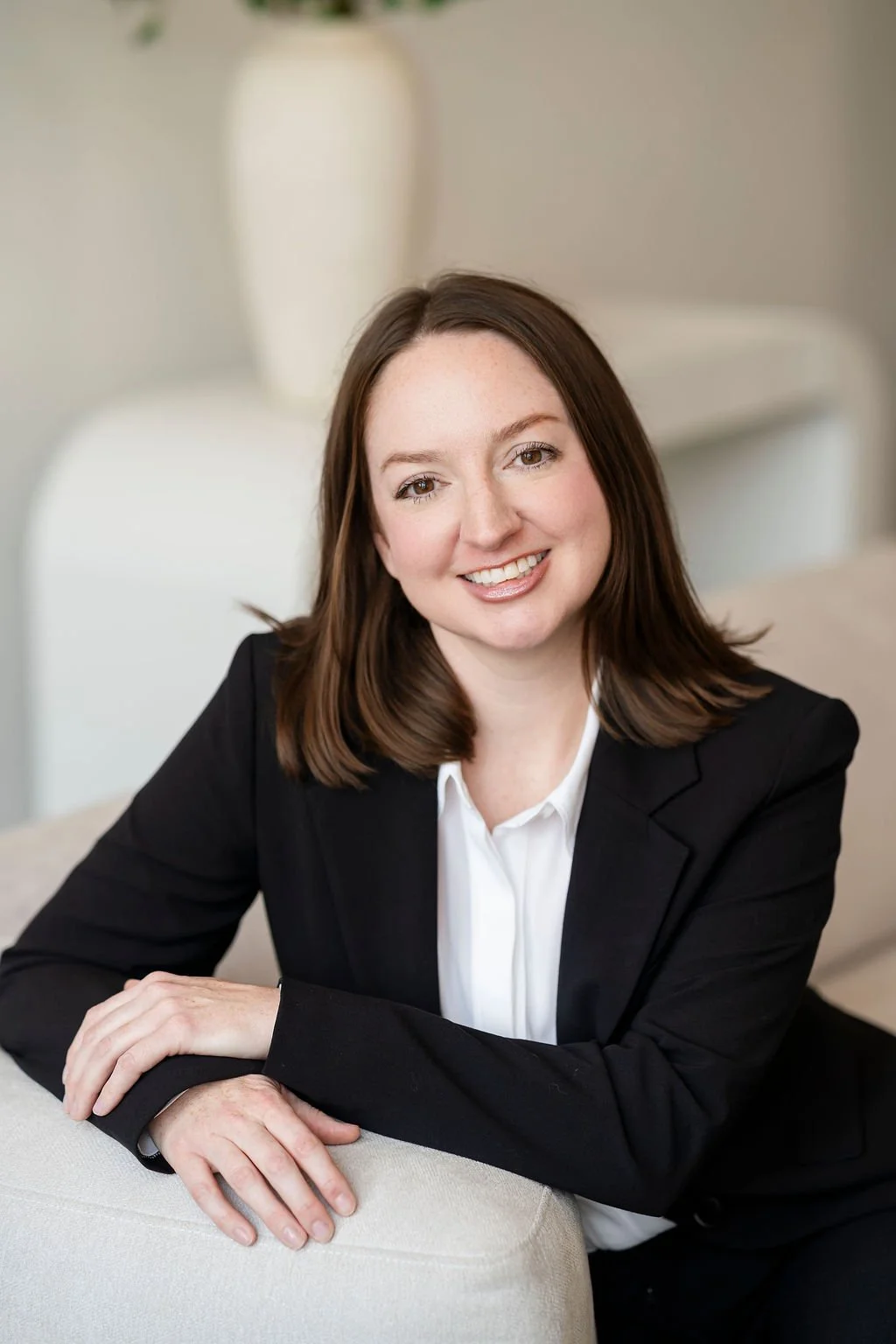 Dr. Mullen, sitting on a white couch, posing and smiling for the camera, wearing a black pantsuit