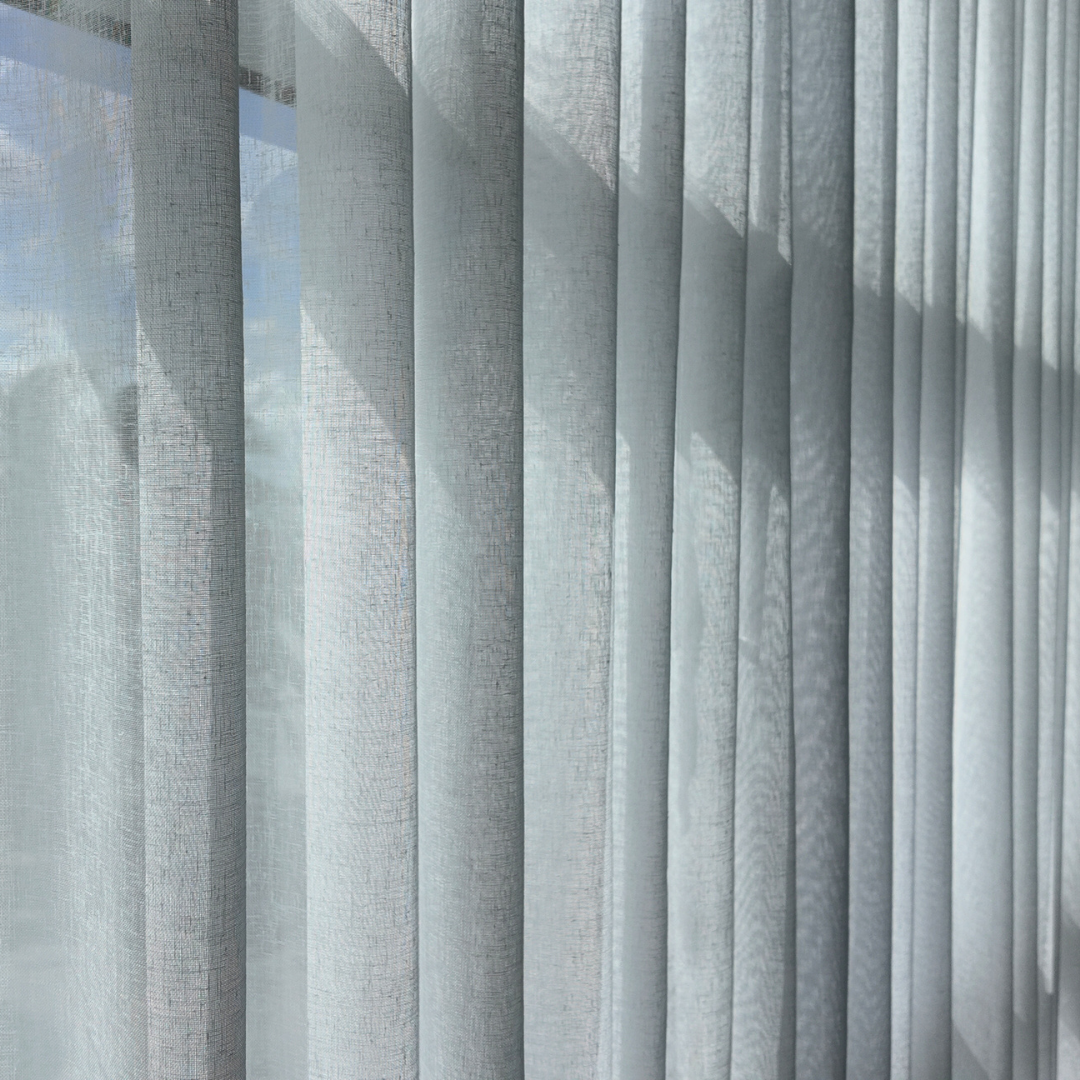 Close-up of sheer white curtains hanging in front of a window, with sunlight casting shadows.