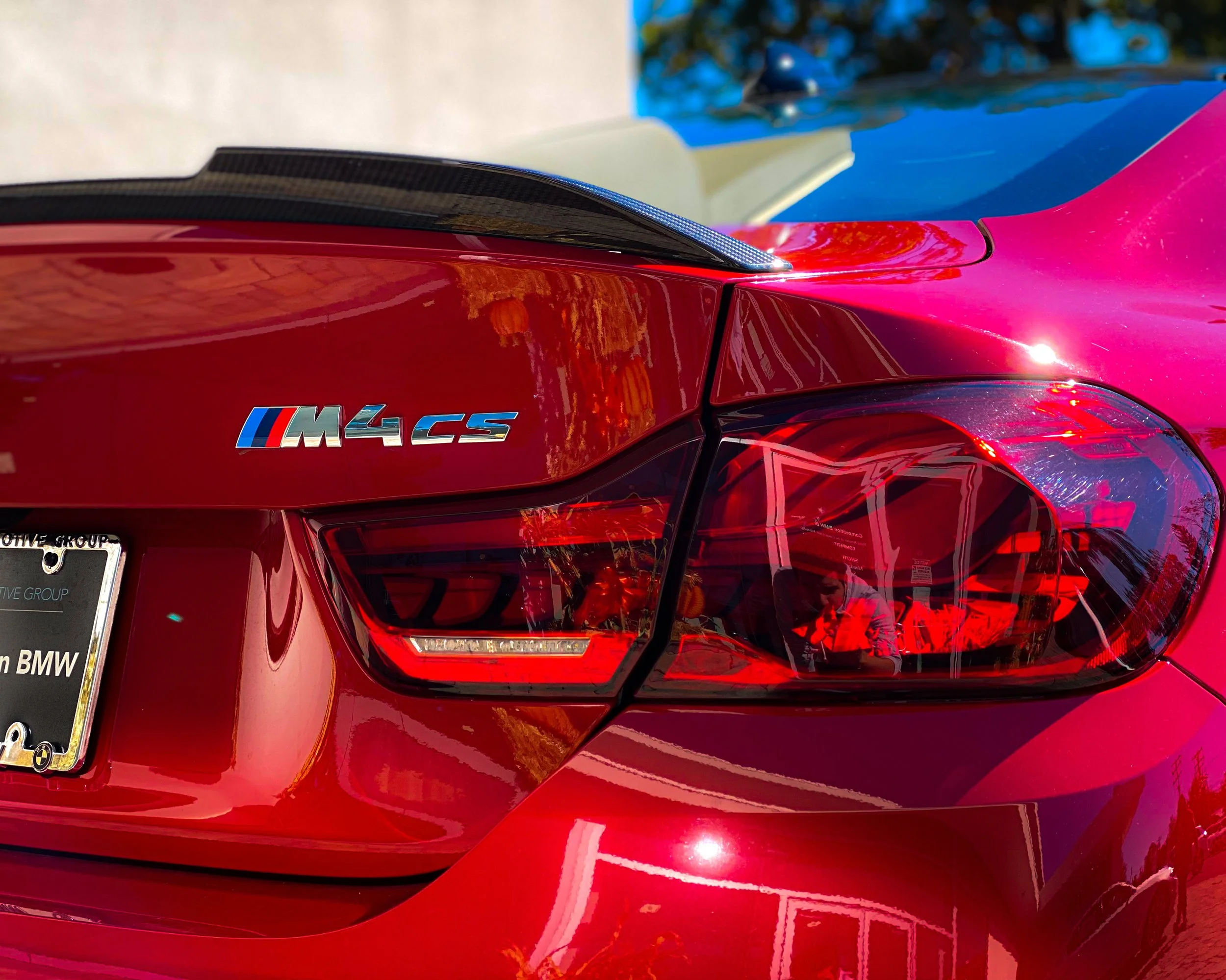Close-up of the rear of a red BMW M4 CS sports car, showing the taillight, part of the rear spoiler, and the M4 CS badge on the trunk.