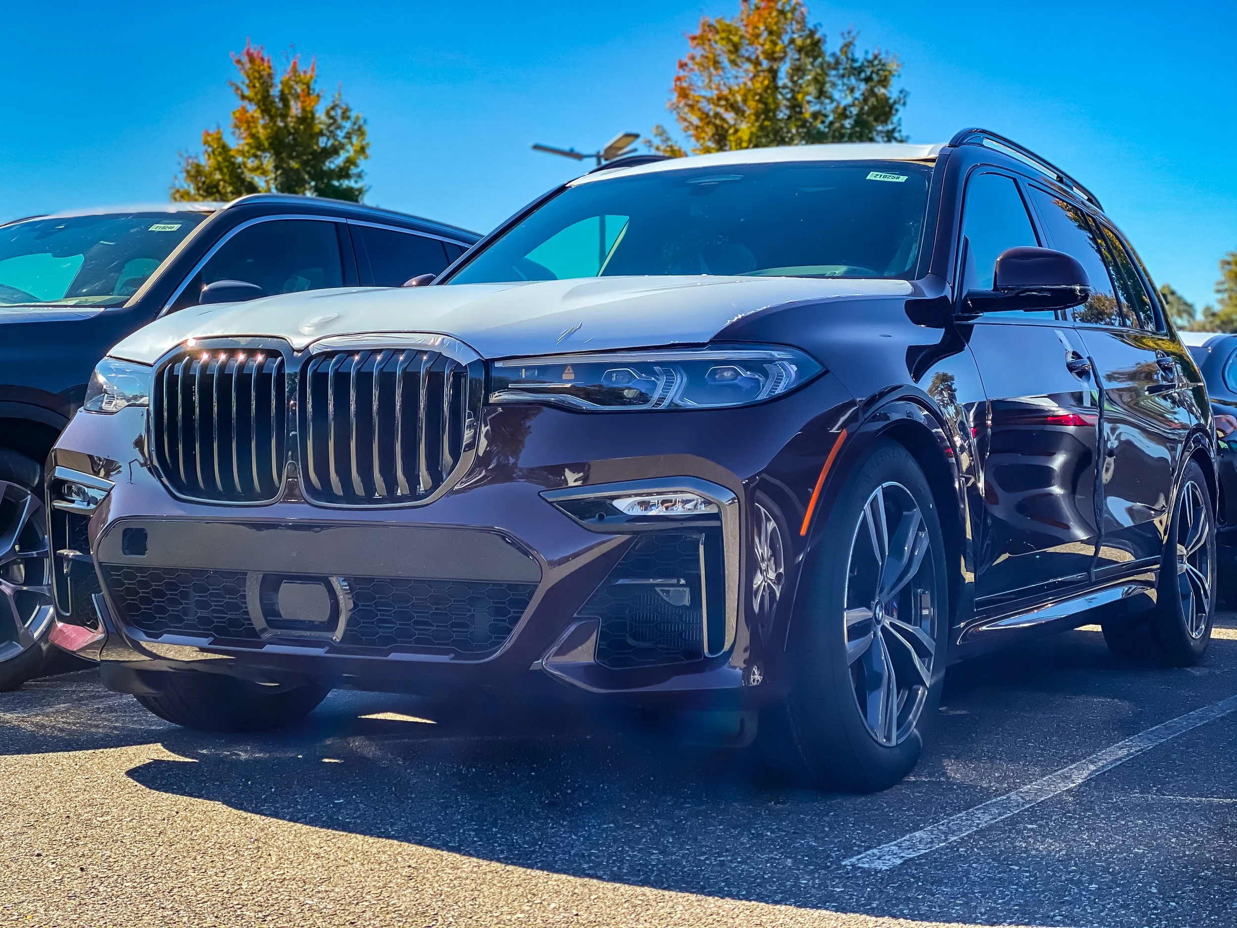 A black luxury SUV parked in a lot with other vehicles, trees, and a blue sky in the background.