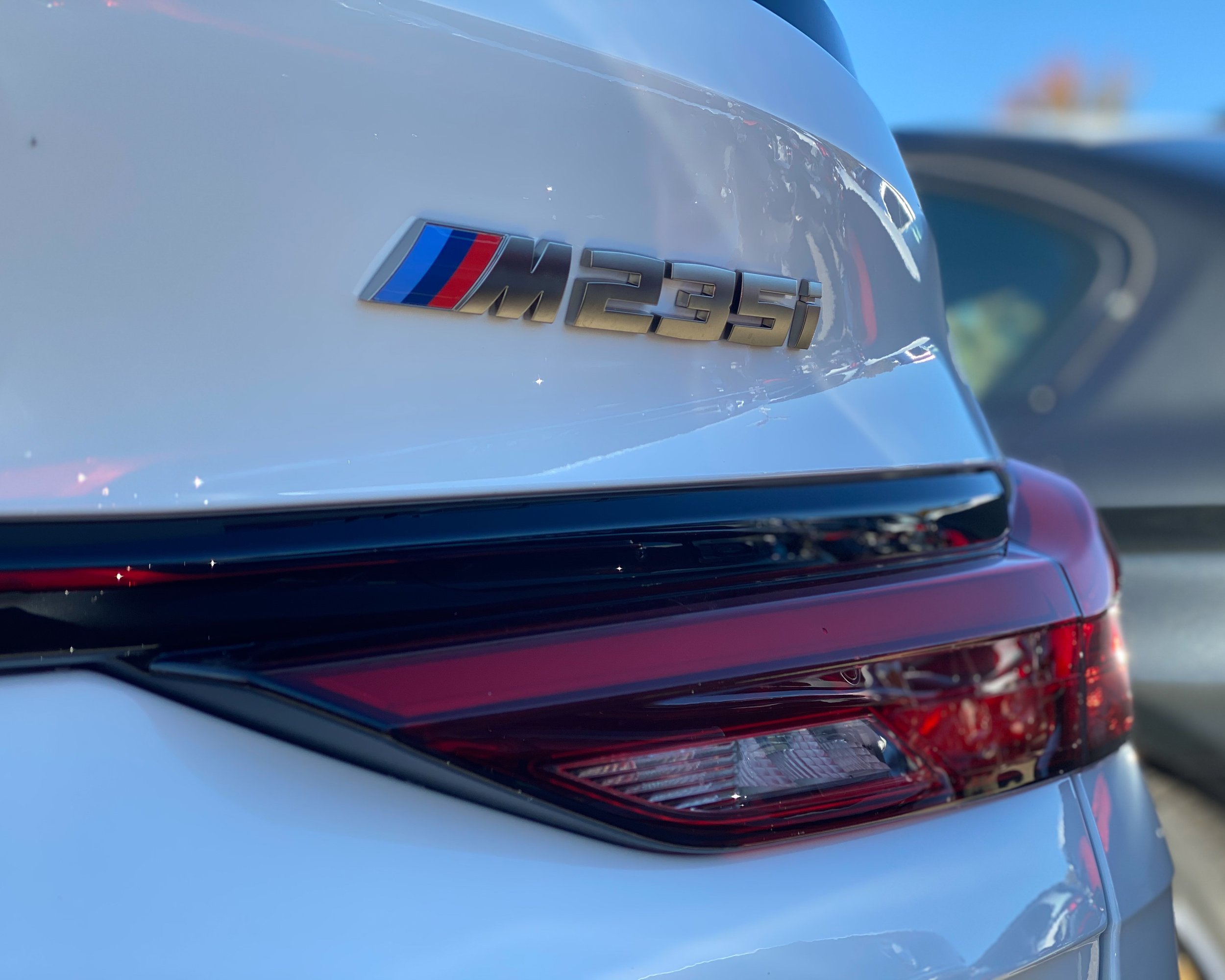 Close-up of the rear section of a white BMW M235i car, showing its badge and tail light.