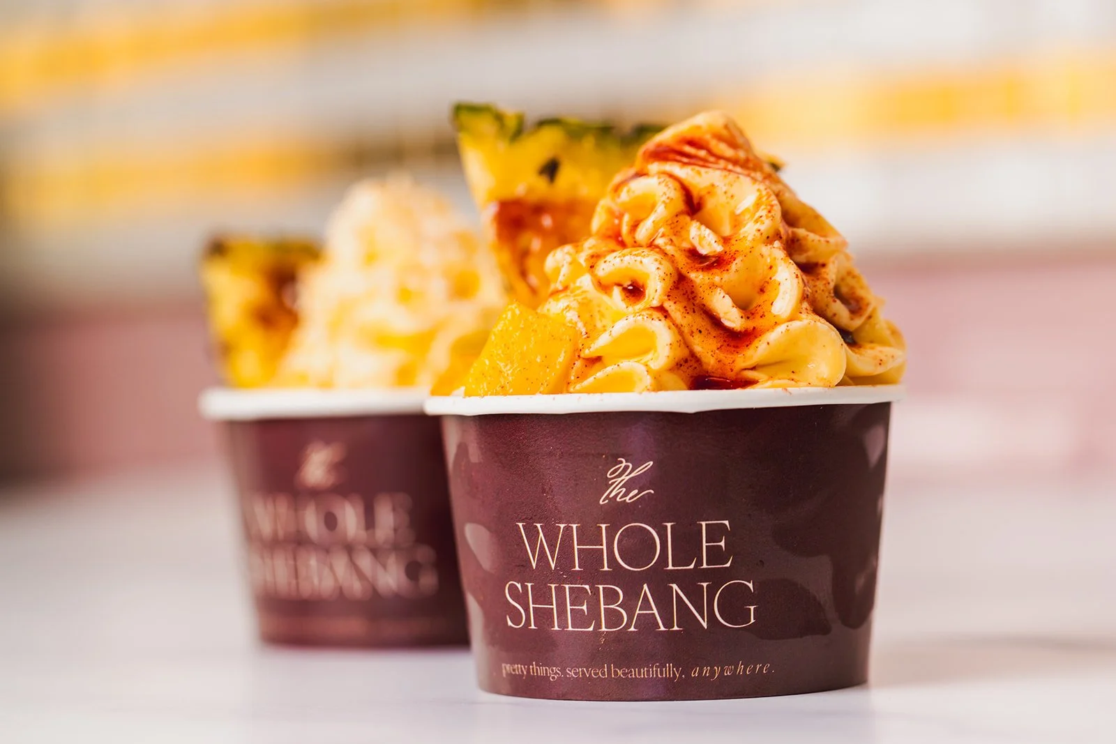 Two cups of Dole Whip with chunks of mango and sprinkled with plum sugar and toasted coconut, titled "The Whole Shebang".