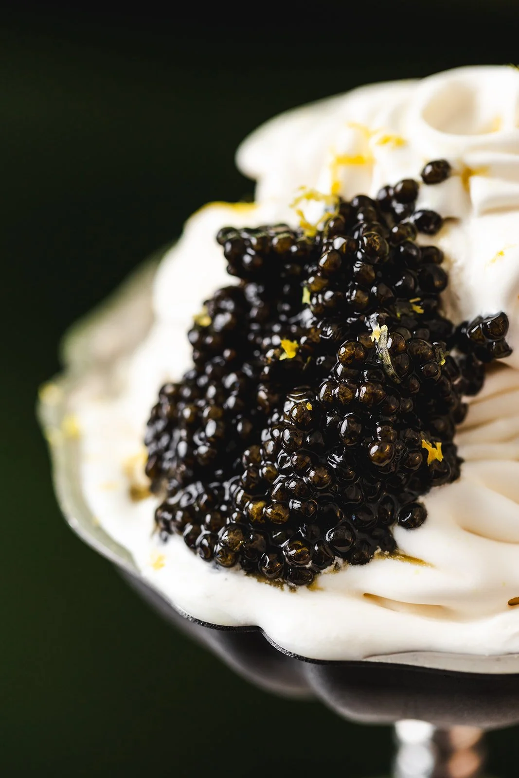 Close-up of a dessert topped with black caviar and lemon zest, with whipped cream underneath.