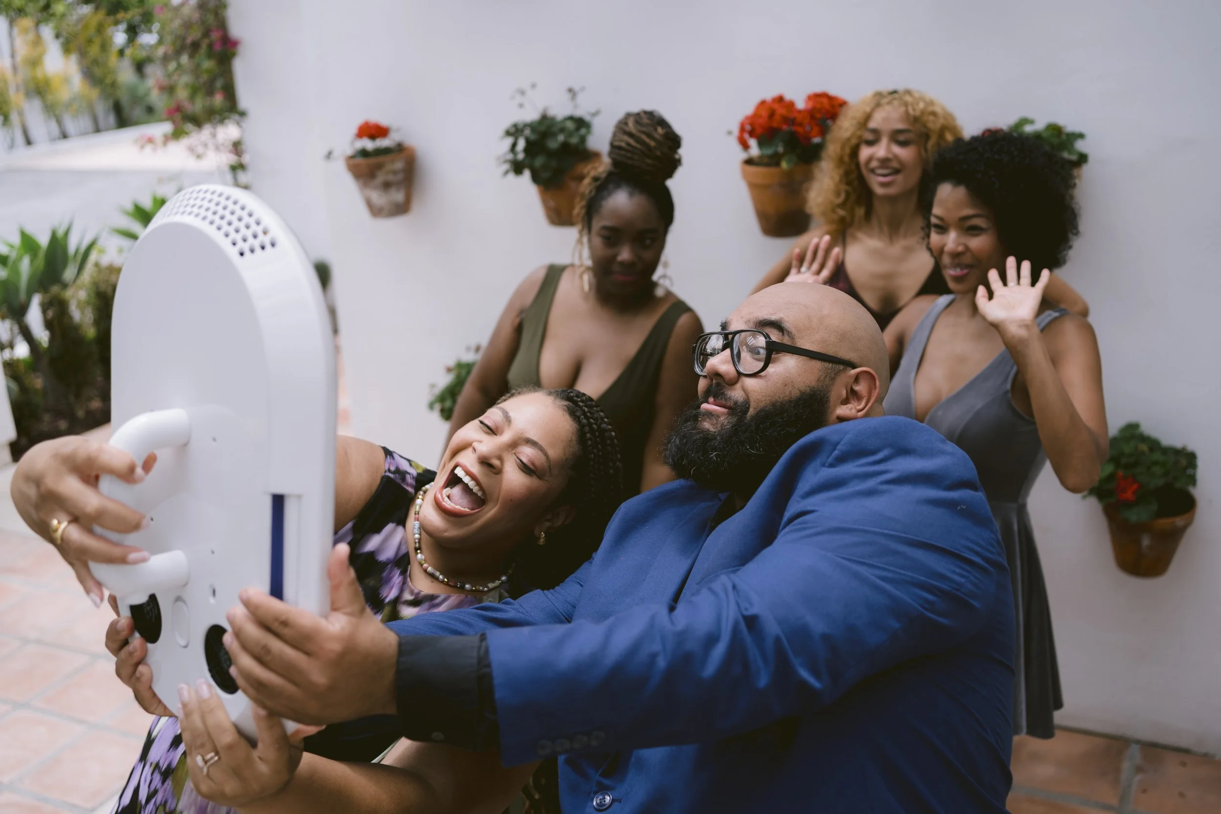 A group of five friends taking a selfie together outdoors, with three women in and behind the group and one woman and one man holding the phone. They are smiling and appear to be having fun.