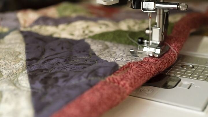 Close-up of a sewing machine stitching colorful quilt fabric with a red border.