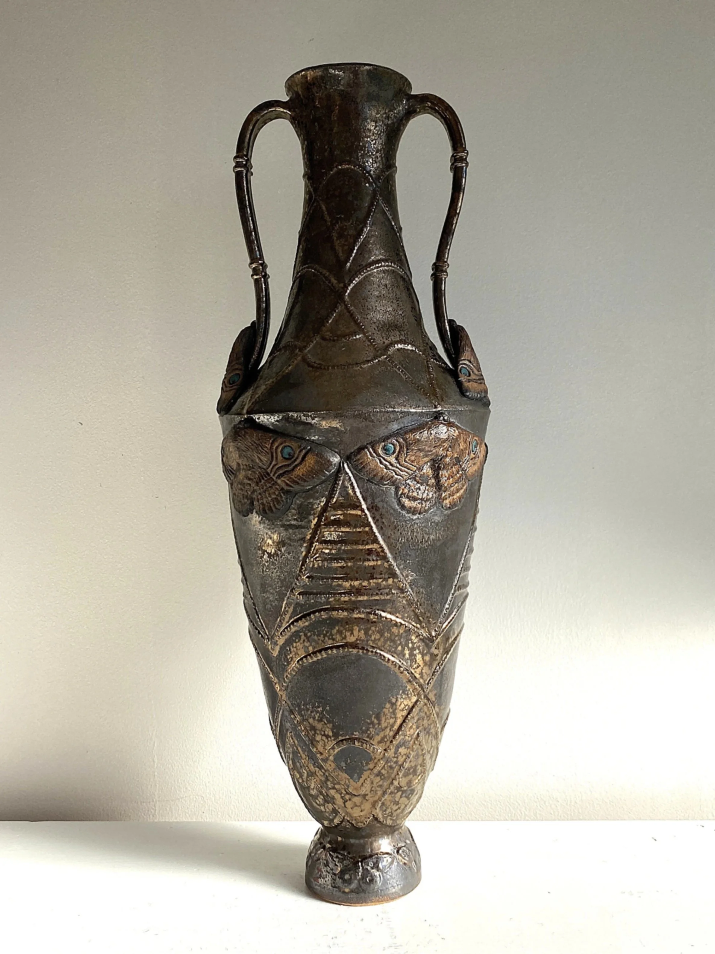 An ornate metal vase with a textured surface, featuring engraved butterfly and geometric patterns, and two curved handles.