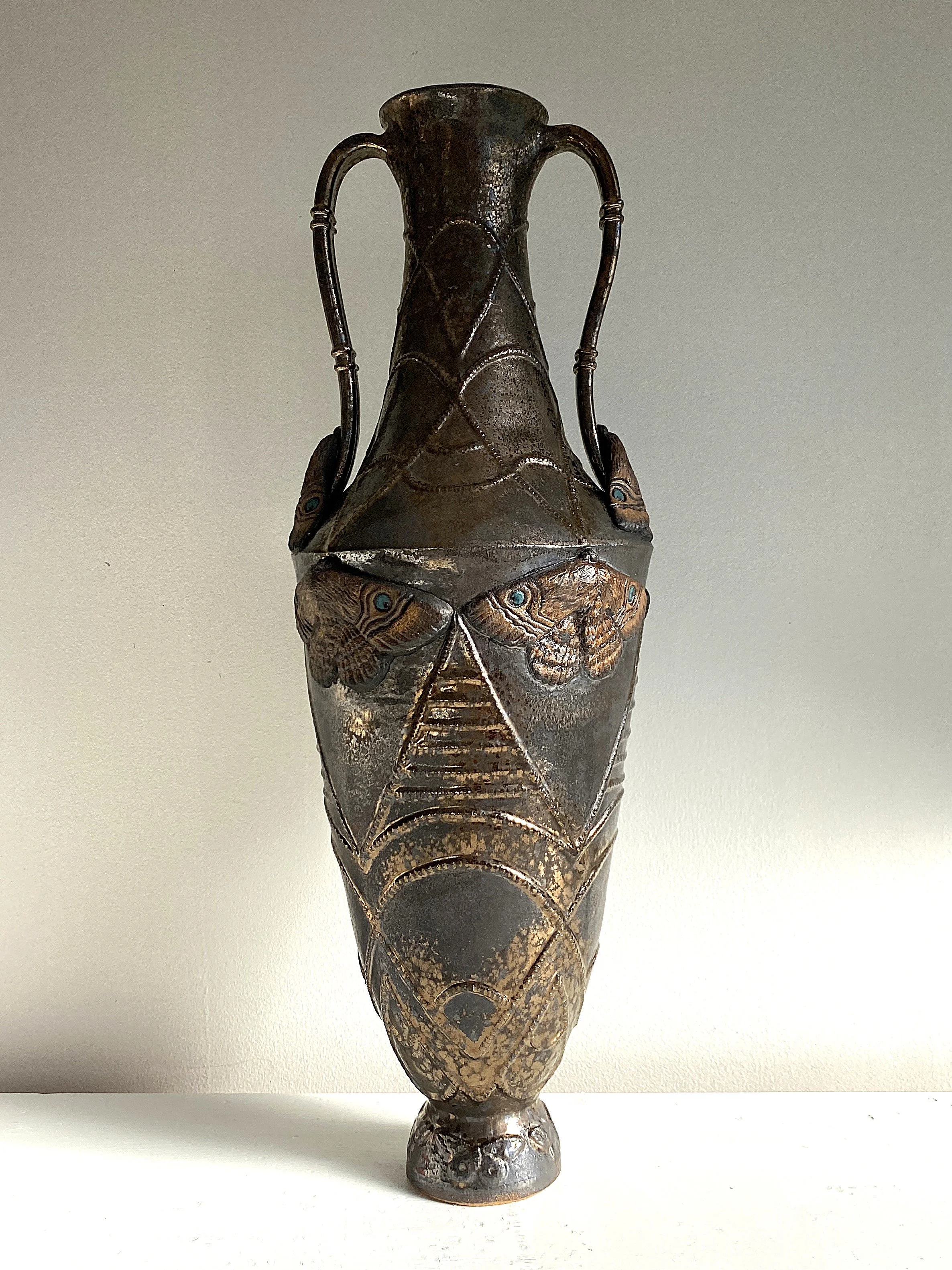 Decorative metal vase with carved butterfly and geometric patterns, two curved handles, and a narrow base.